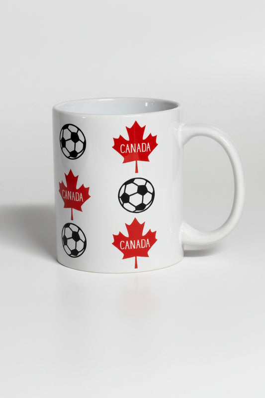 White ceramic mug printed with red maple leaves and soccer balls, representing Canada’s love for the beautiful game.