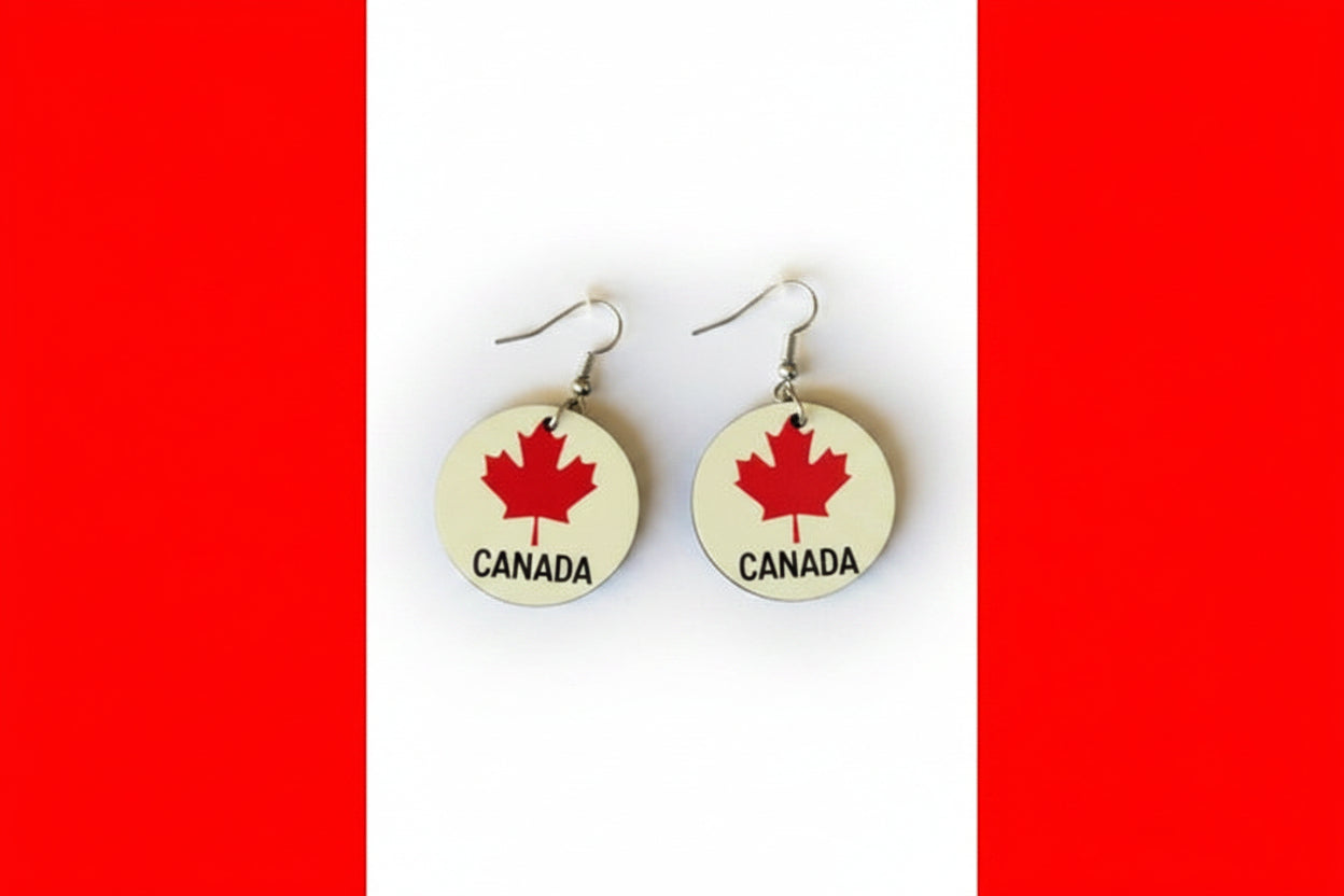 Pair of circular earrings featuring red maple leaves and the word “Canada” printed in black on a white background, displayed on a red and white surface.