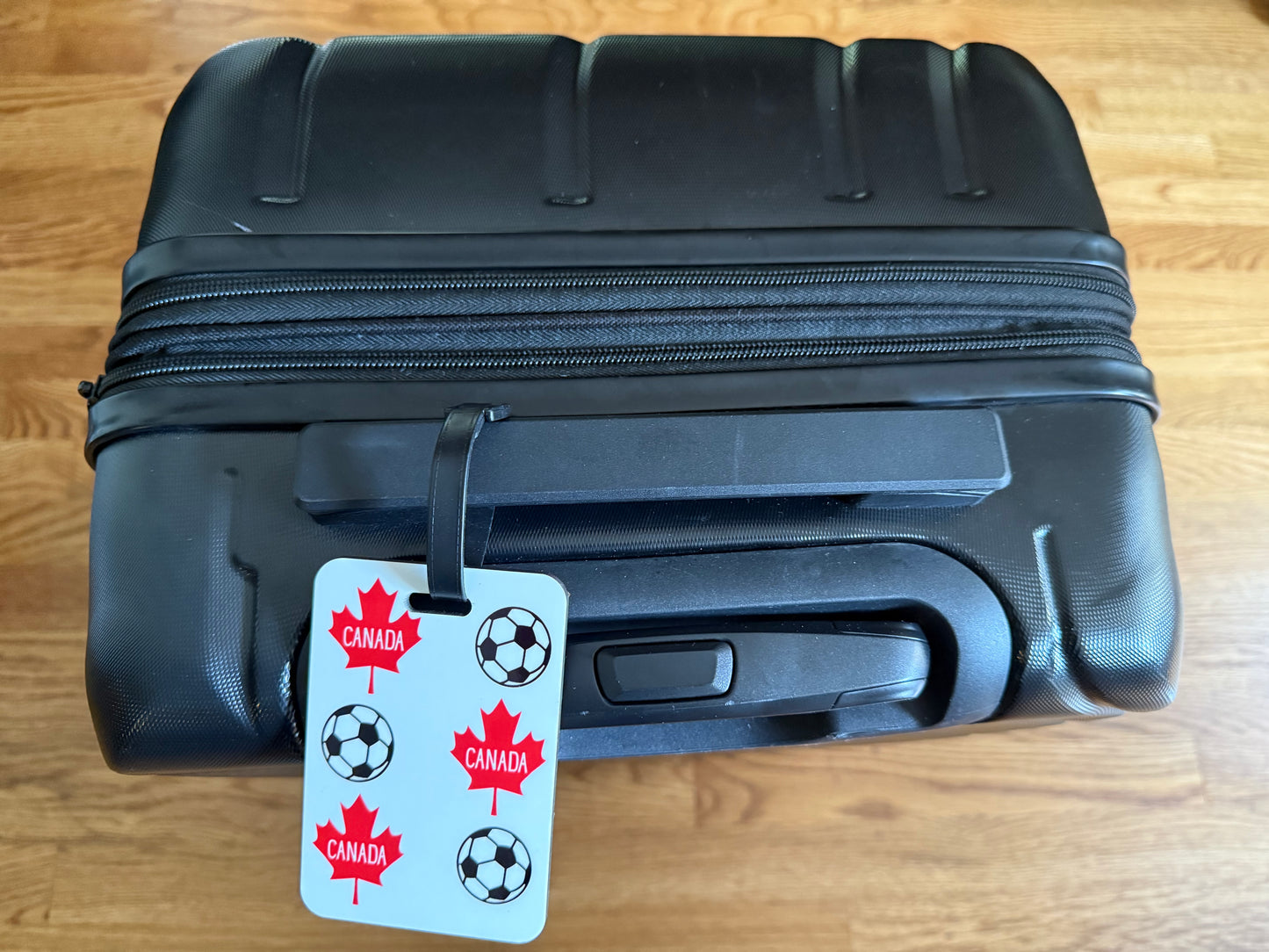 Canada soccer luggage tag with black strap on a black suitcase. Roxzell