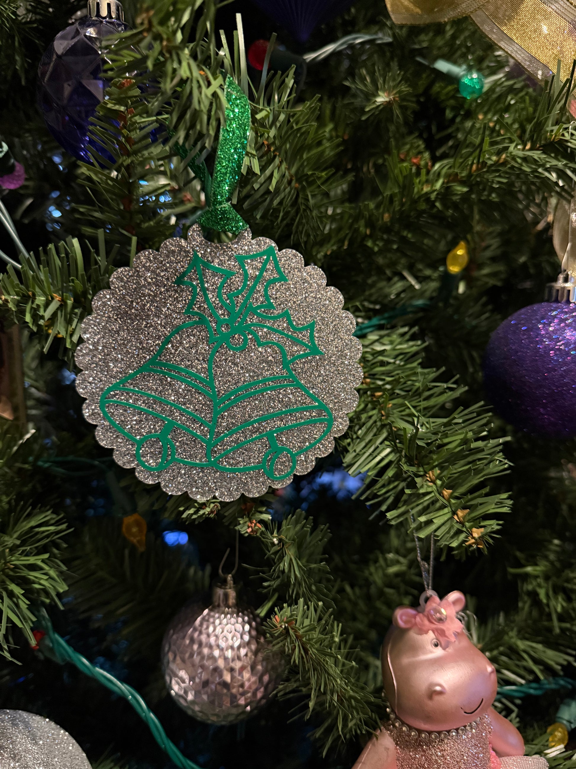 Traditional holiday ornament with green bells and holly outlined on a silver glitter surface. Roxzell