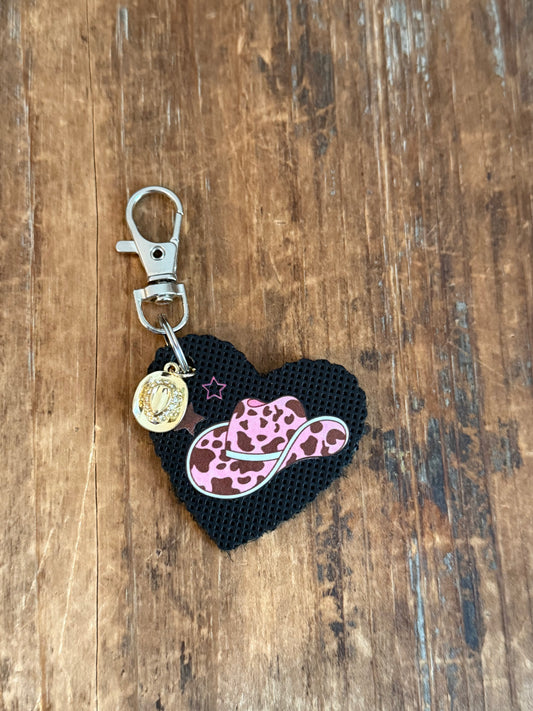 Black heart bag charm with a pink and brown spotted cowgirl hat, star accents, dangling hat charm, and silver-tone clasp