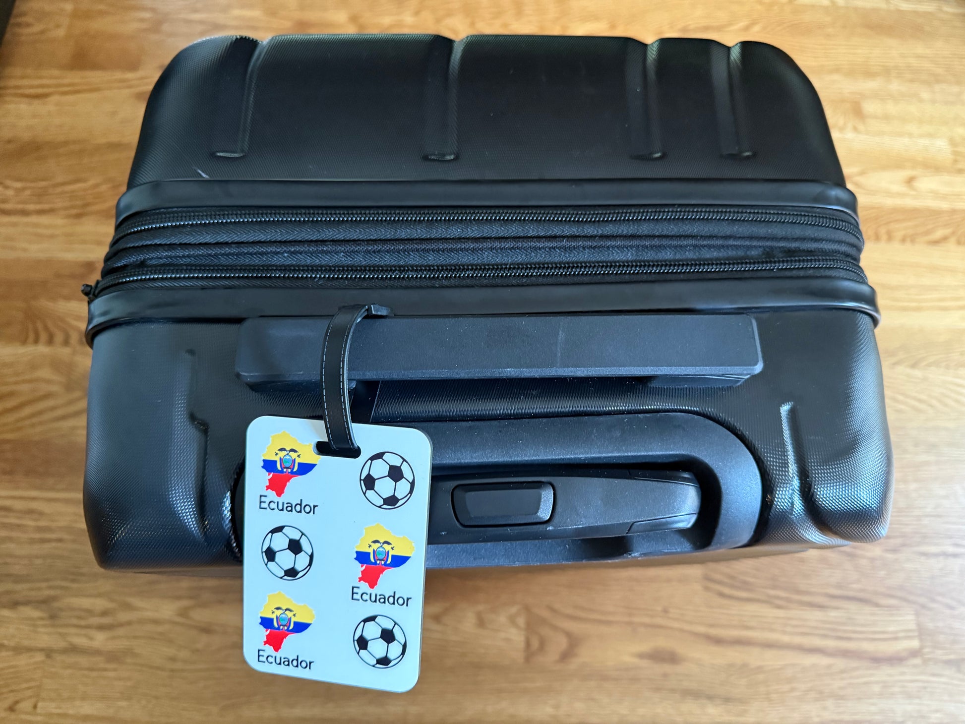 Ecuador map and soccer ball pattern printed on durable luggage tag hanging on a black suitcase.