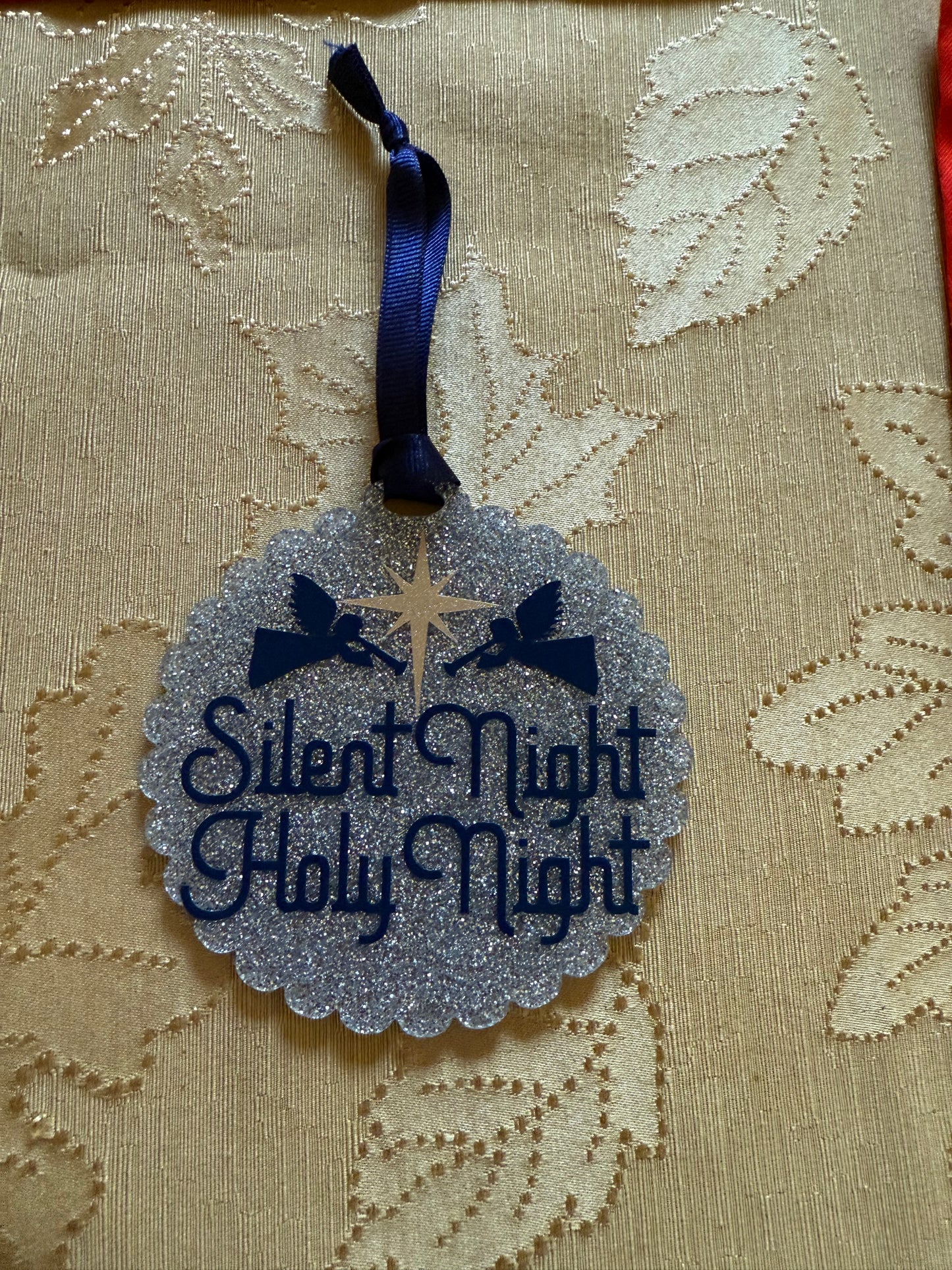 Faith-themed holiday ornament featuring two angels and a golden star on glittery silver background on a gold tablecloth, Roxzell