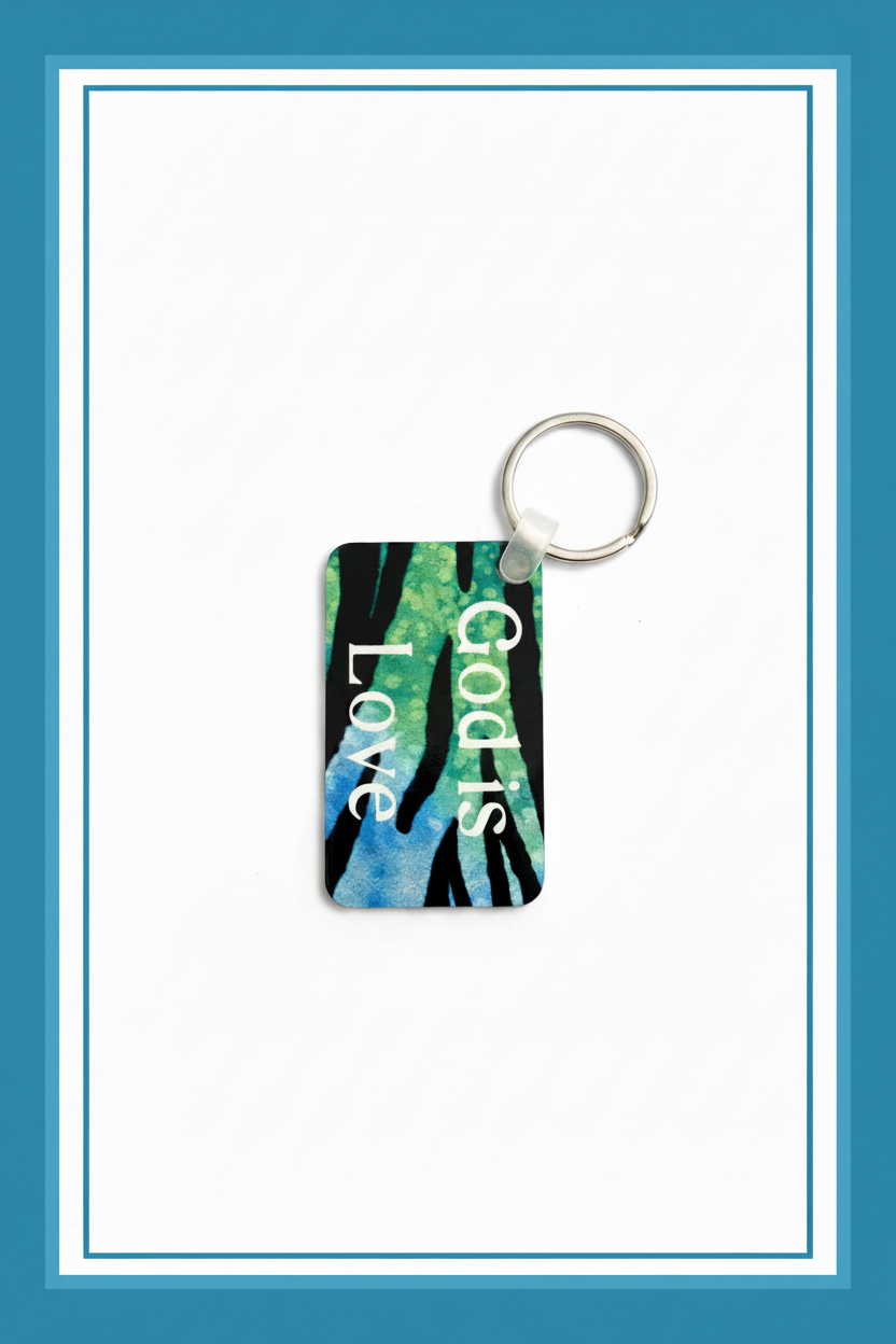 A colorful keychain with green, blue, and black animal print patterns and the words “God is Love” printed vertically in white, resting on a white background with blue border.