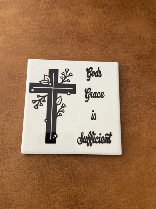 Square white ceramic coaster with black and white cross and words "God's Grace is Sufficient".