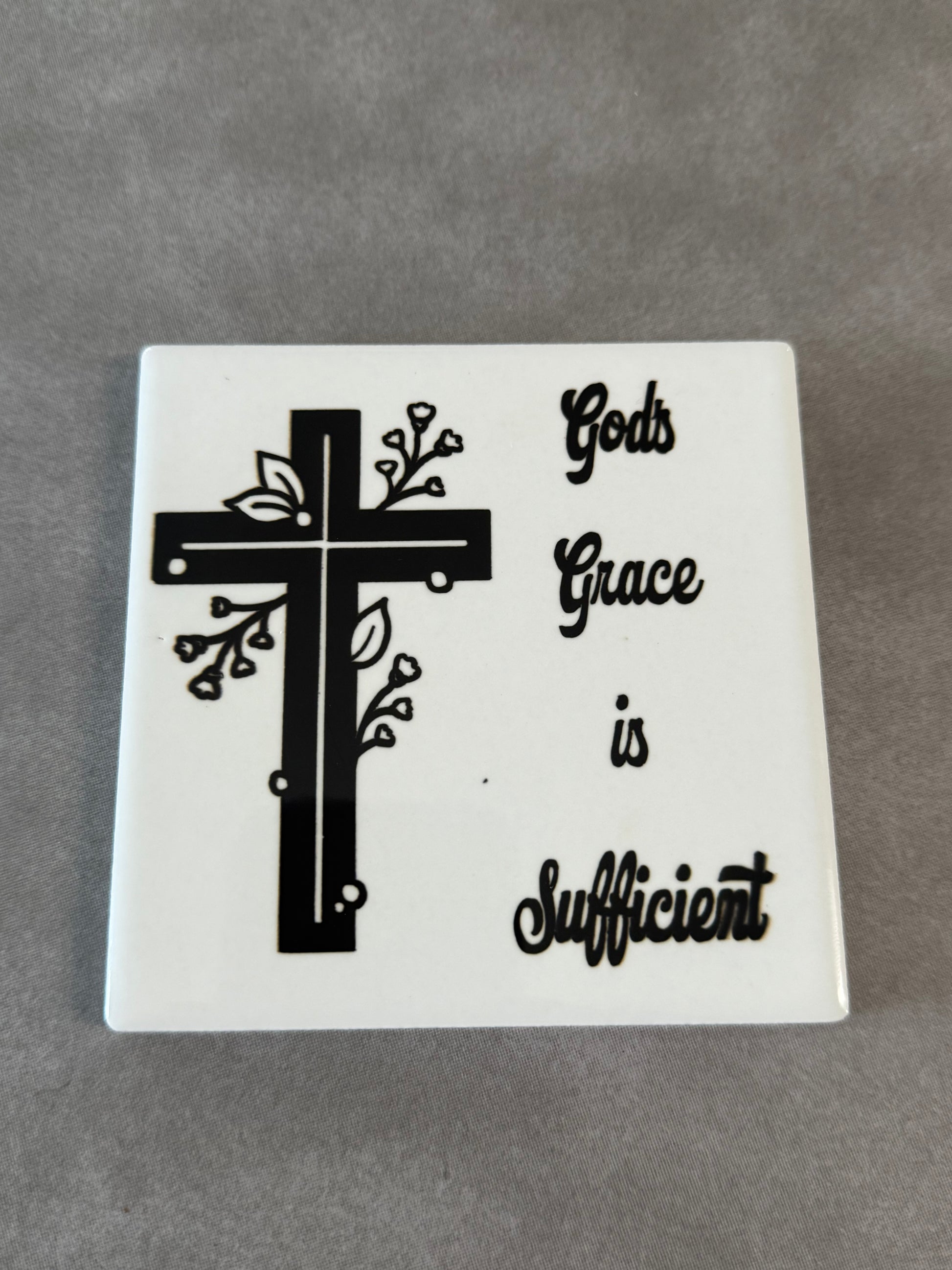 Square white ceramic coaster with black and white cross and words "God's Grace is Sufficient".