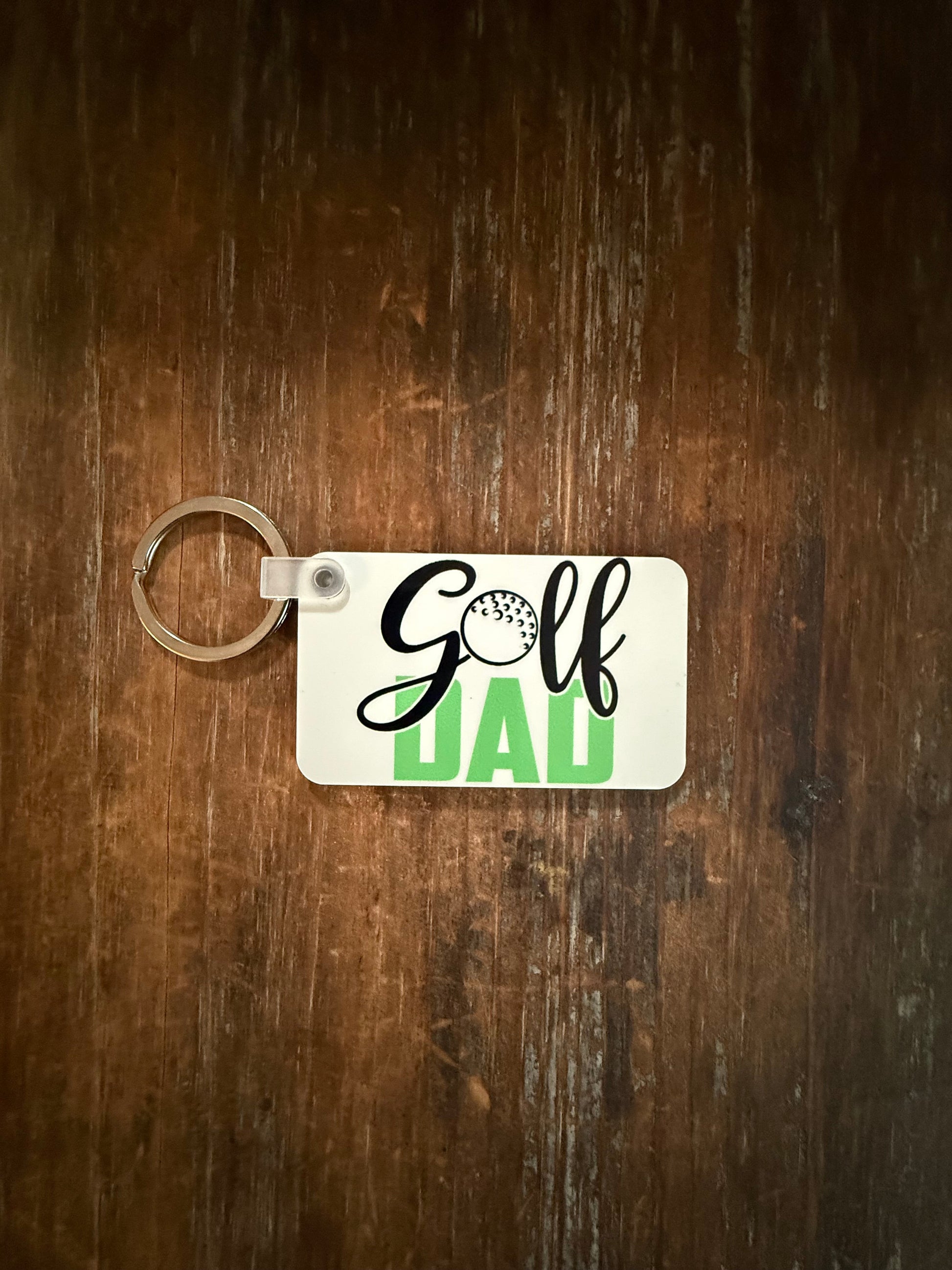 White keychain with “Golf Dad” design featuring golf ball accent and green lettering. Roxzell
