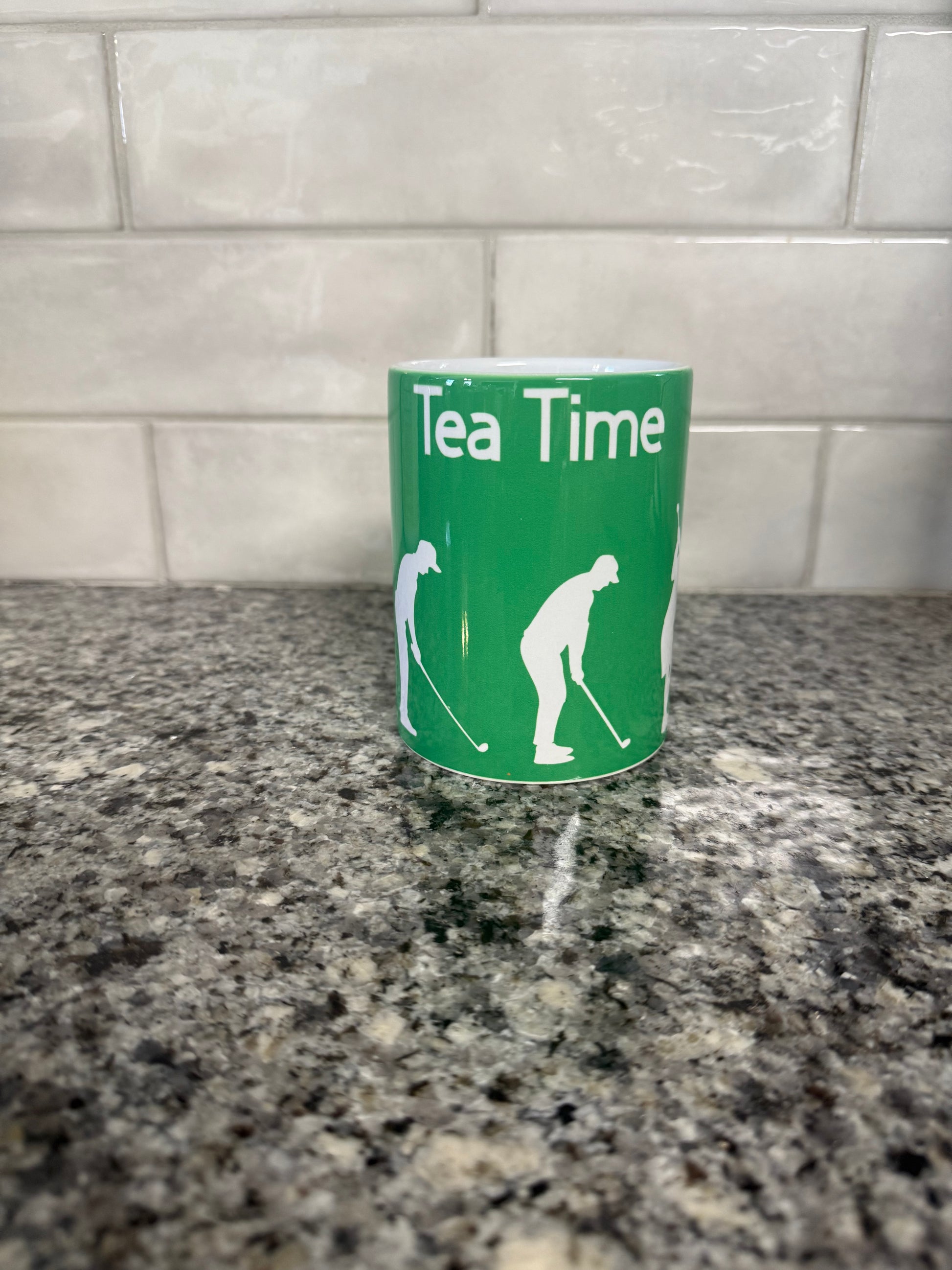 Ceramic mug with 'Tea Time' text and golf-themed illustrations, displayed against a kitchen backdrop.
