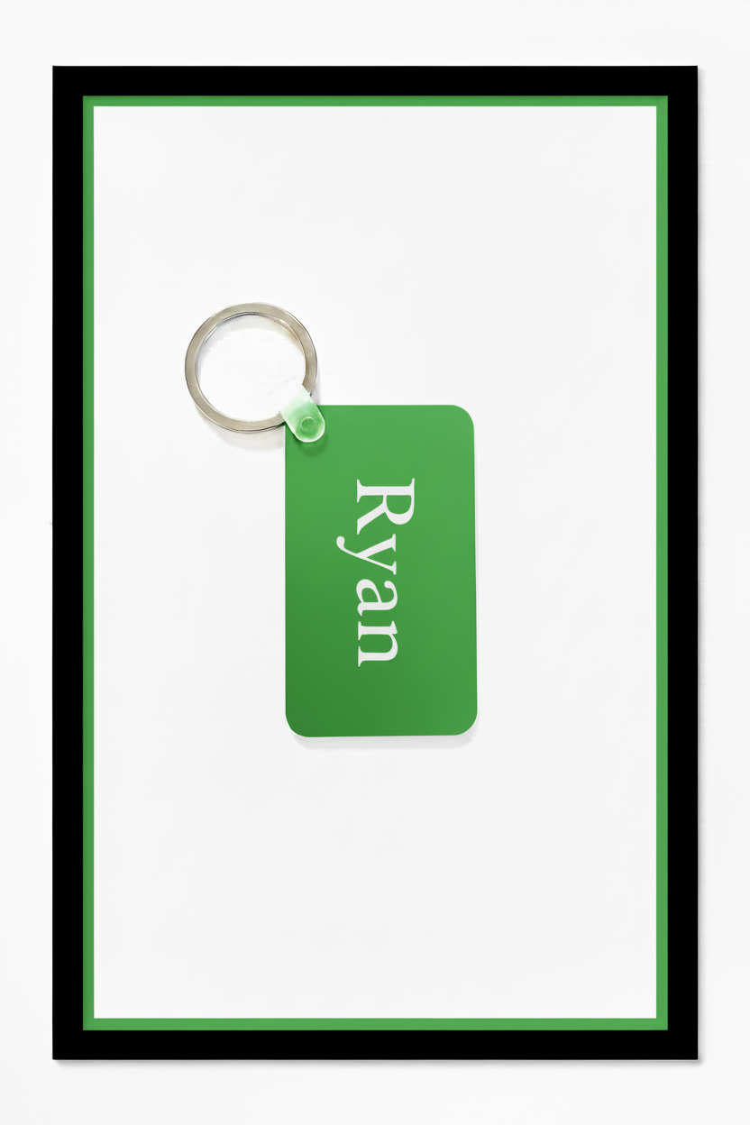 A personalized green rectangular keychain tag with the name 'Ryan' printed in white serif text, attached to a silver metal key ring, set against a white background with a green inner border and black outer frame. Roxzell