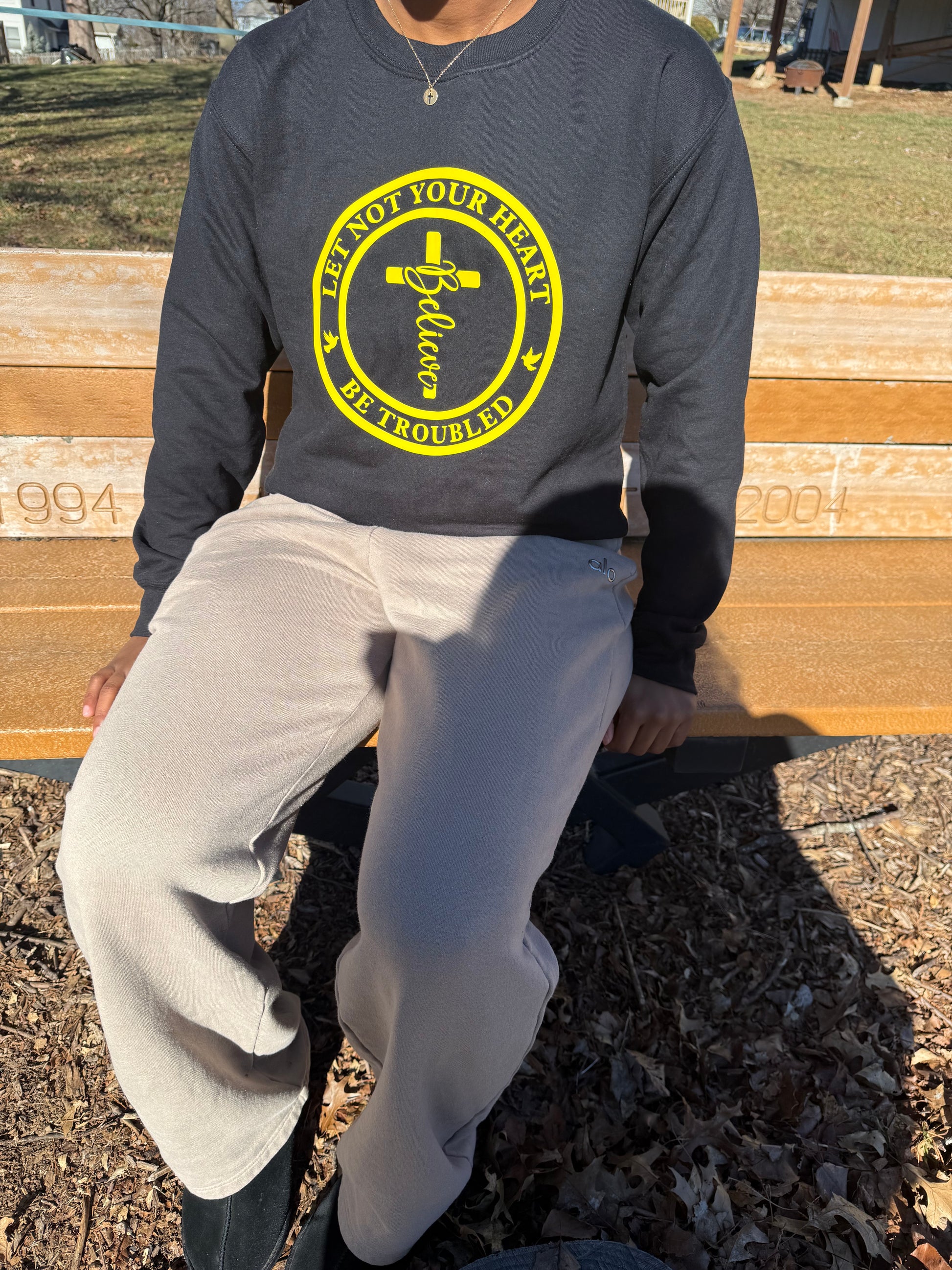 Detailed view of yellow cross, “Believe” script, and dove icons on a black sweatshirt, Roxzell