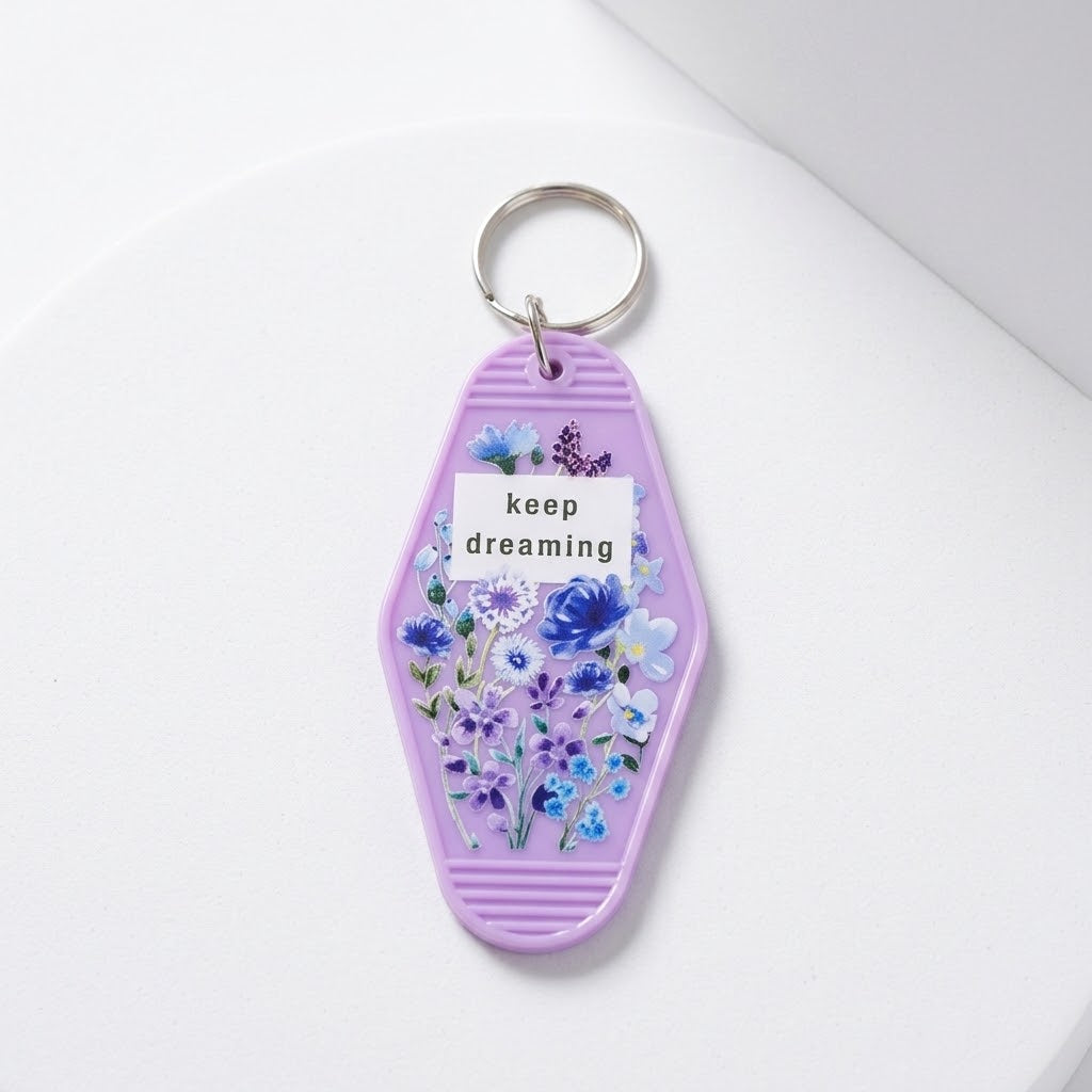 A lavender coffin-shaped keychain with a floral illustration and the words 'keep dreaming' printed on it, attached to a silver metal key ring, set against a clean white background. Roxzell