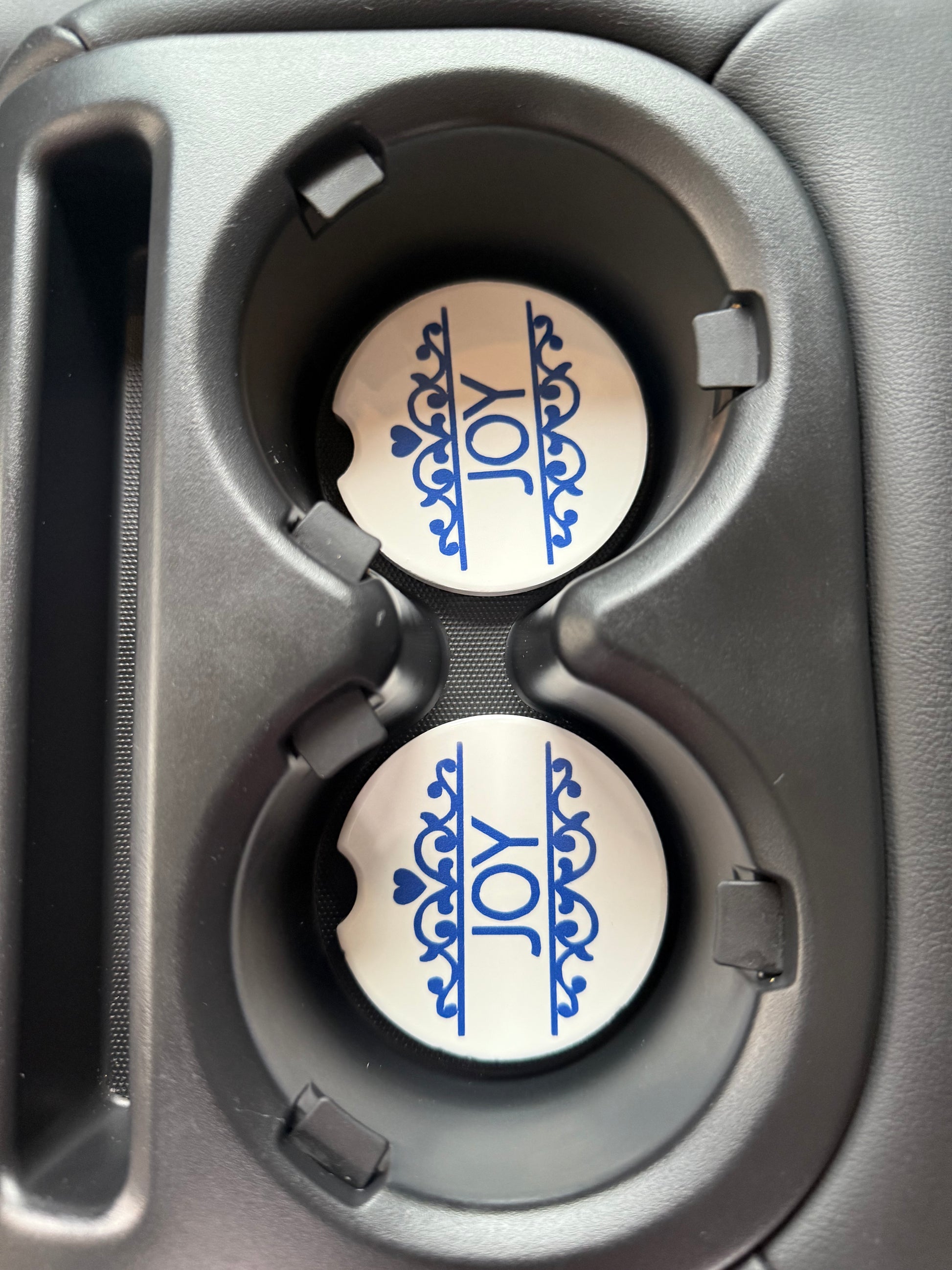 Two car coasters with 'JOY' design in a cup holder.