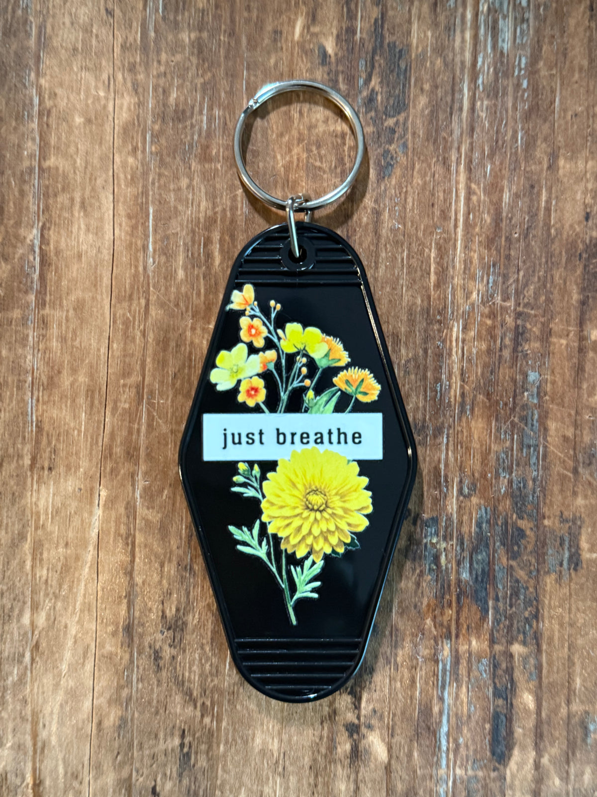 Black "Just Breathe"motel-style keychain with yellow floral artwork. Roxzell