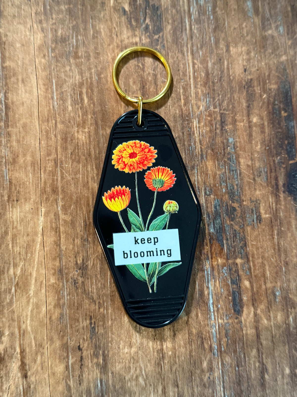 Black Keep Blooming motel-style keychain with orange and yellow flowers