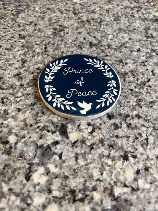 Kitchen table-top drink coaster.  Coaster is midnight blue designed with the words "Prince of Peace", leaves and a dove, all in white.