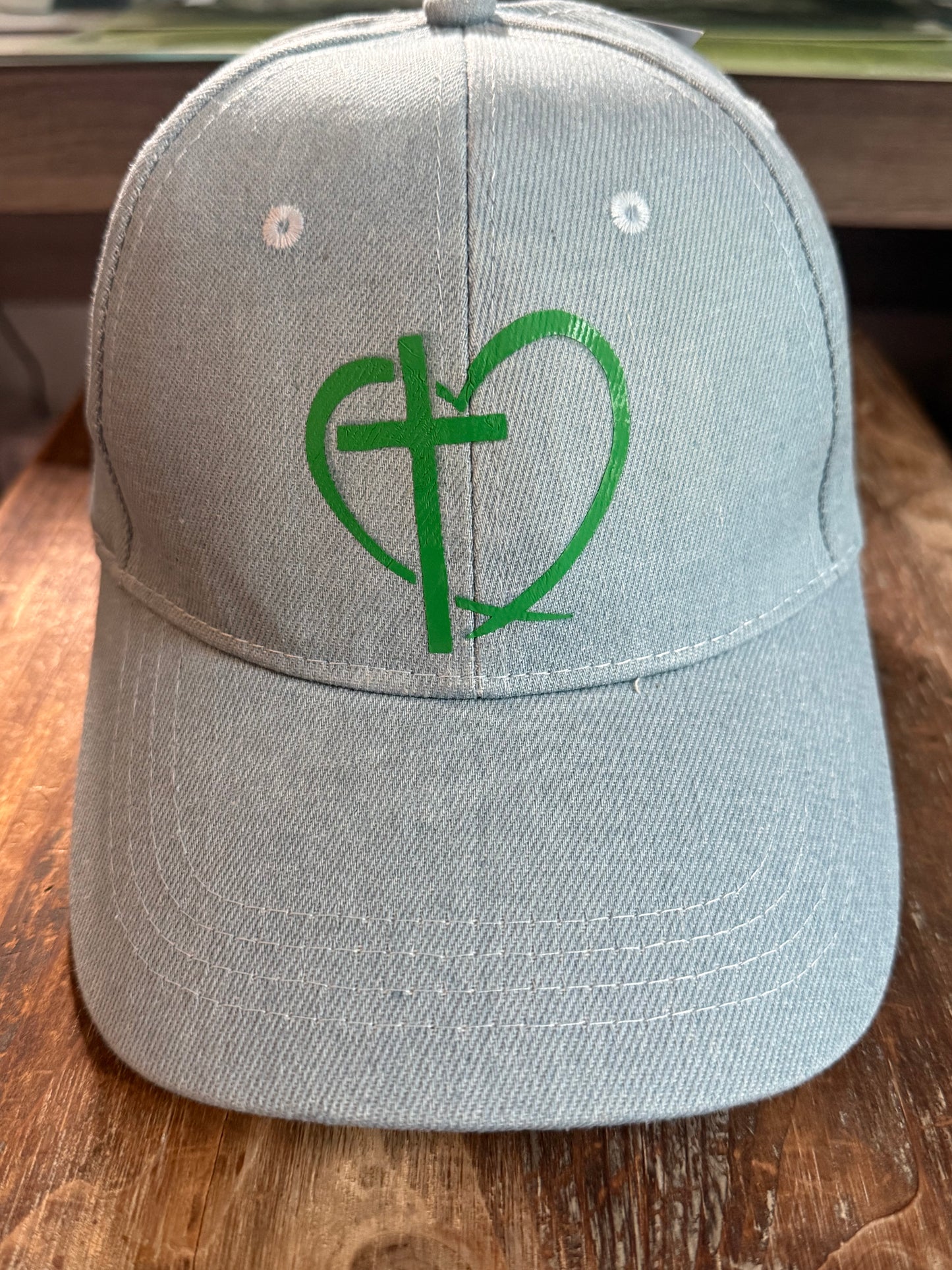 Light blue denim cap with green cross and heart design on a wood surface.  Roxzell