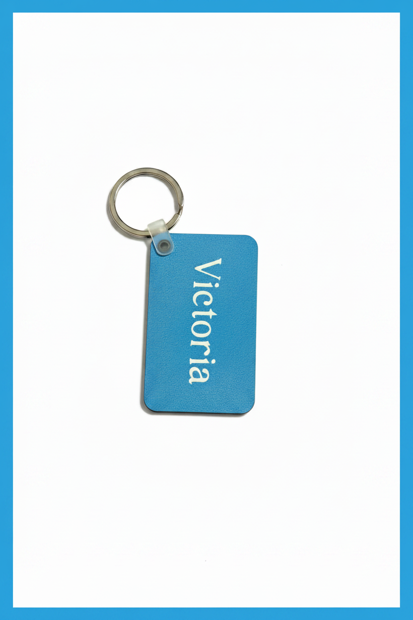 A rectangular light blue keychain tag with the name 'Victoria' printed vertically in white, attached to a silver metal key ring, shown on a white background with a blue border.