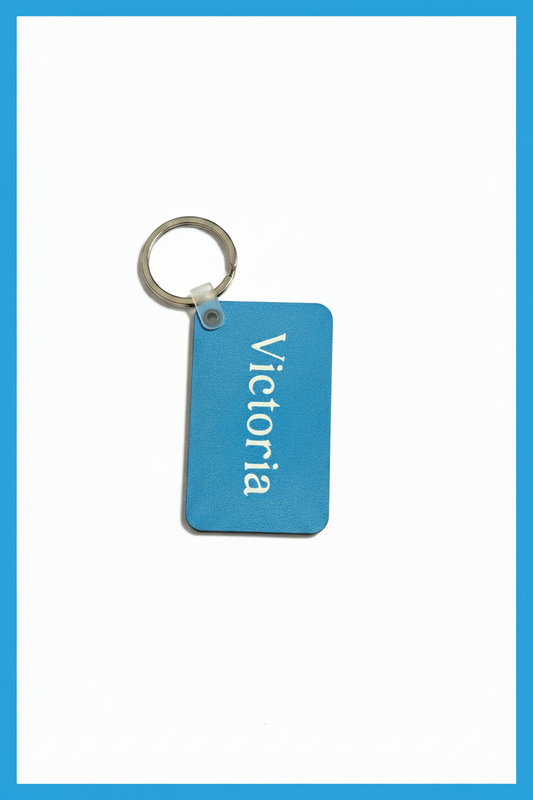 A rectangular light blue keychain tag with the name 'Victoria' printed vertically in white, attached to a silver metal key ring, shown on a white background with a blue border.