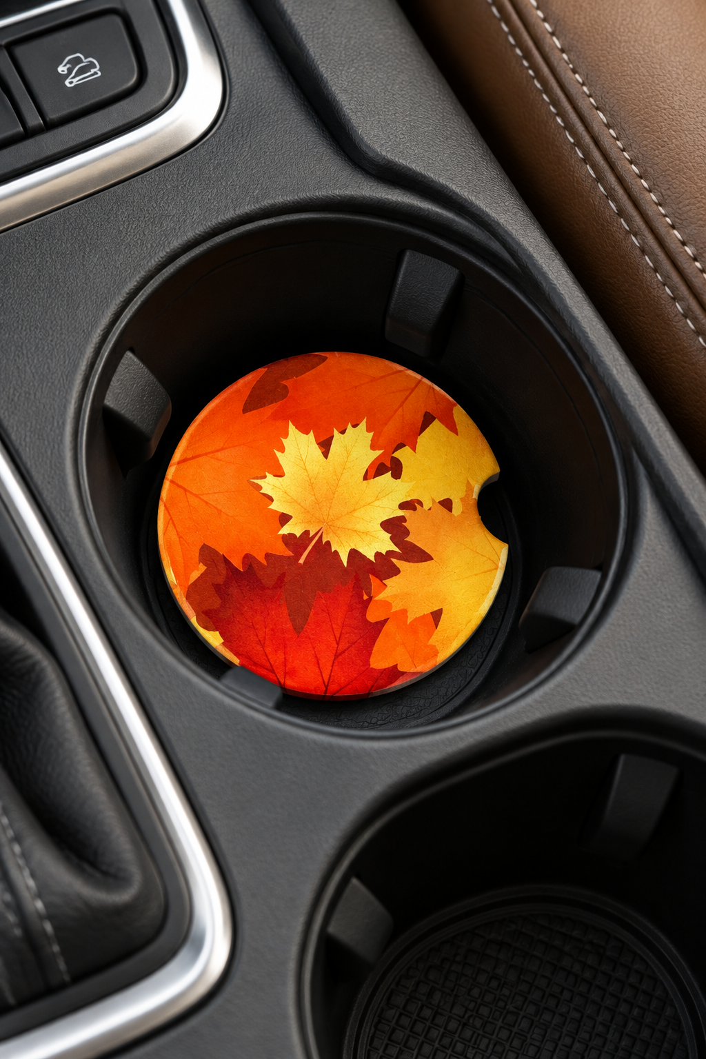 A round car cup holder coaster featuring a printed design of autumn maple leaves in orange, yellow, and red, resting in a black car console cup holder.