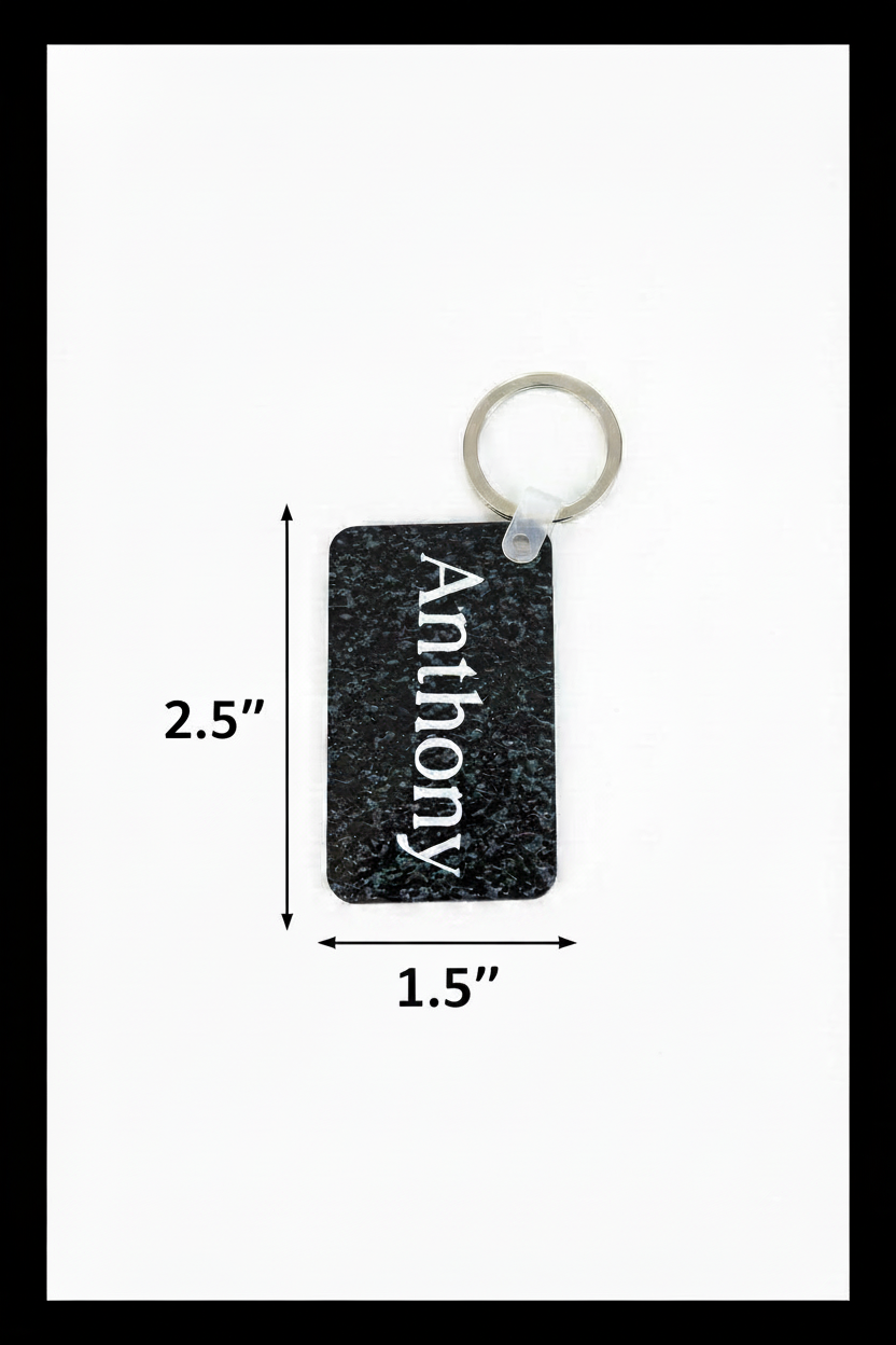 A rectangular black textured keychain with the name 'Anthony' printed vertically in white, attached to a silver metal key ring. A vertical dimension marker on the left indicates a height of 2.5" and a horizontal dimension marker below the keychain indicates 1.5". Roxzell