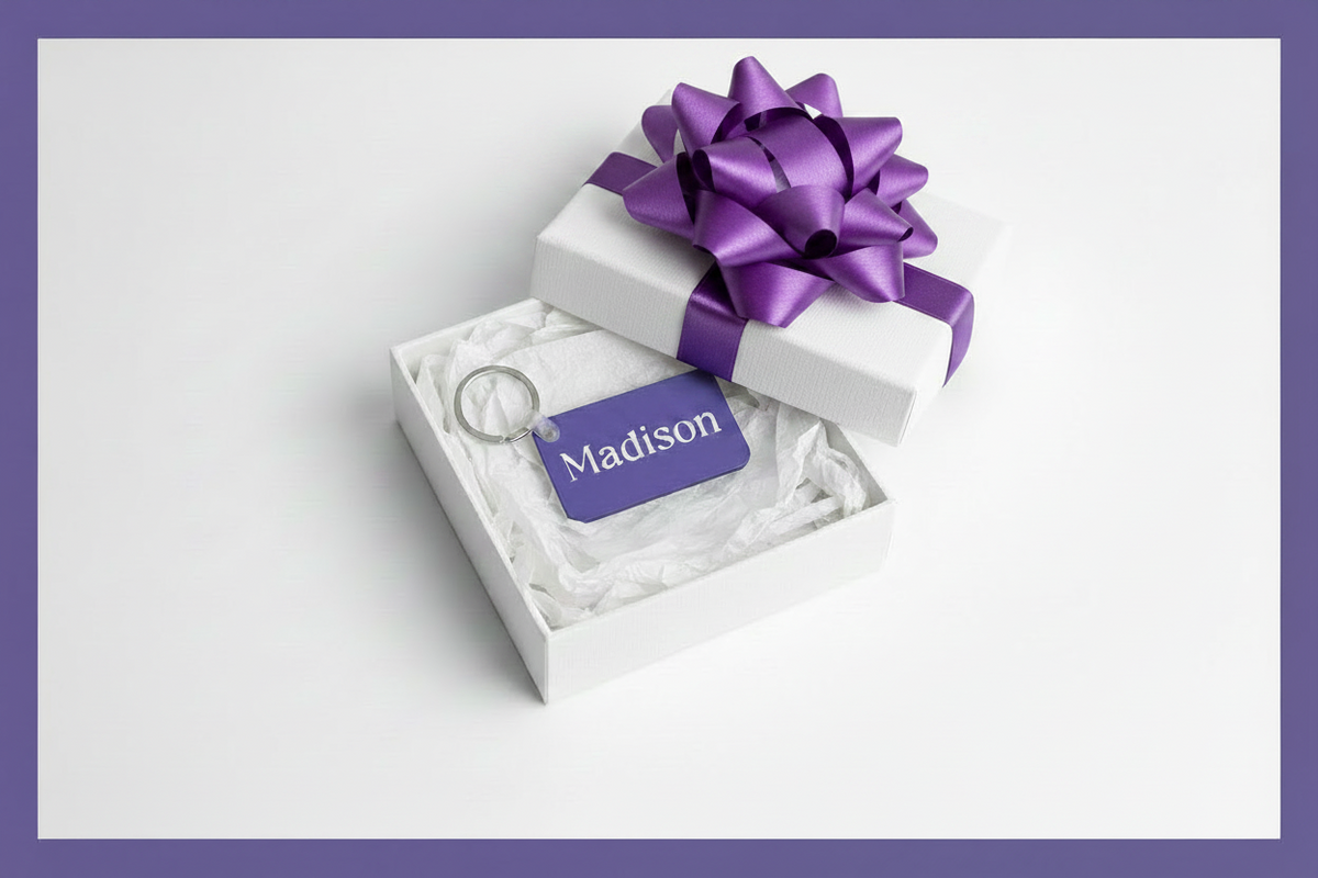 Personalized keychain with name Madison in white print in a white gift box with a purple bow.  Gift is on a white background with a purple border. Roxzell
