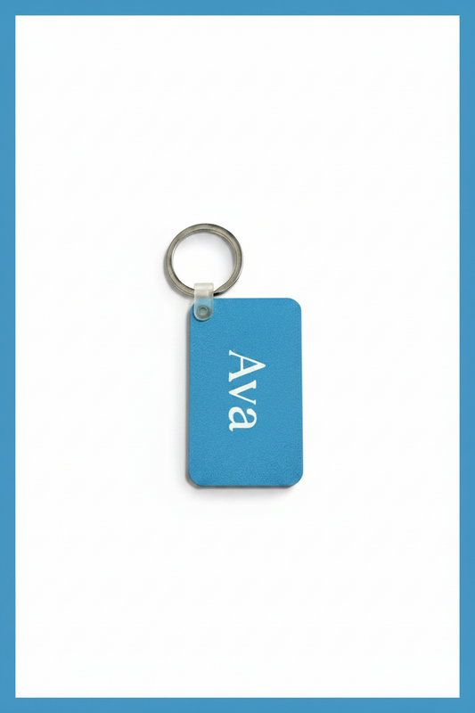 A rectangular blue keychain tag with rounded corners, featuring the name 'Ava' printed vertically in white, attached to a silver metal key ring, set against a white background with a blue border.