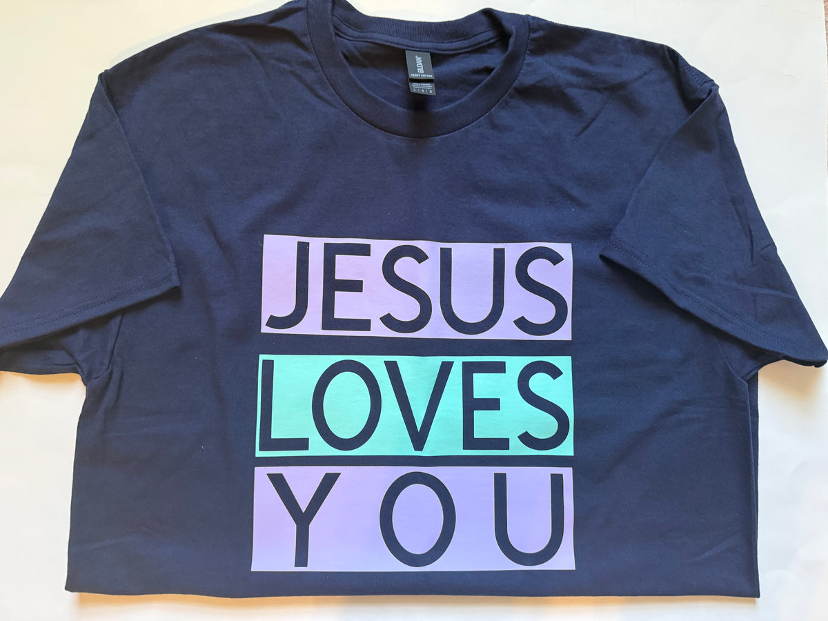 A navy blue short-sleeve t-shirt laid flat on a light beige background, featuring a graphic print that reads 'JESUS LOVES YOU' in black block letters across three stacked lilac and mint green rectangular blocks. Roxzell
