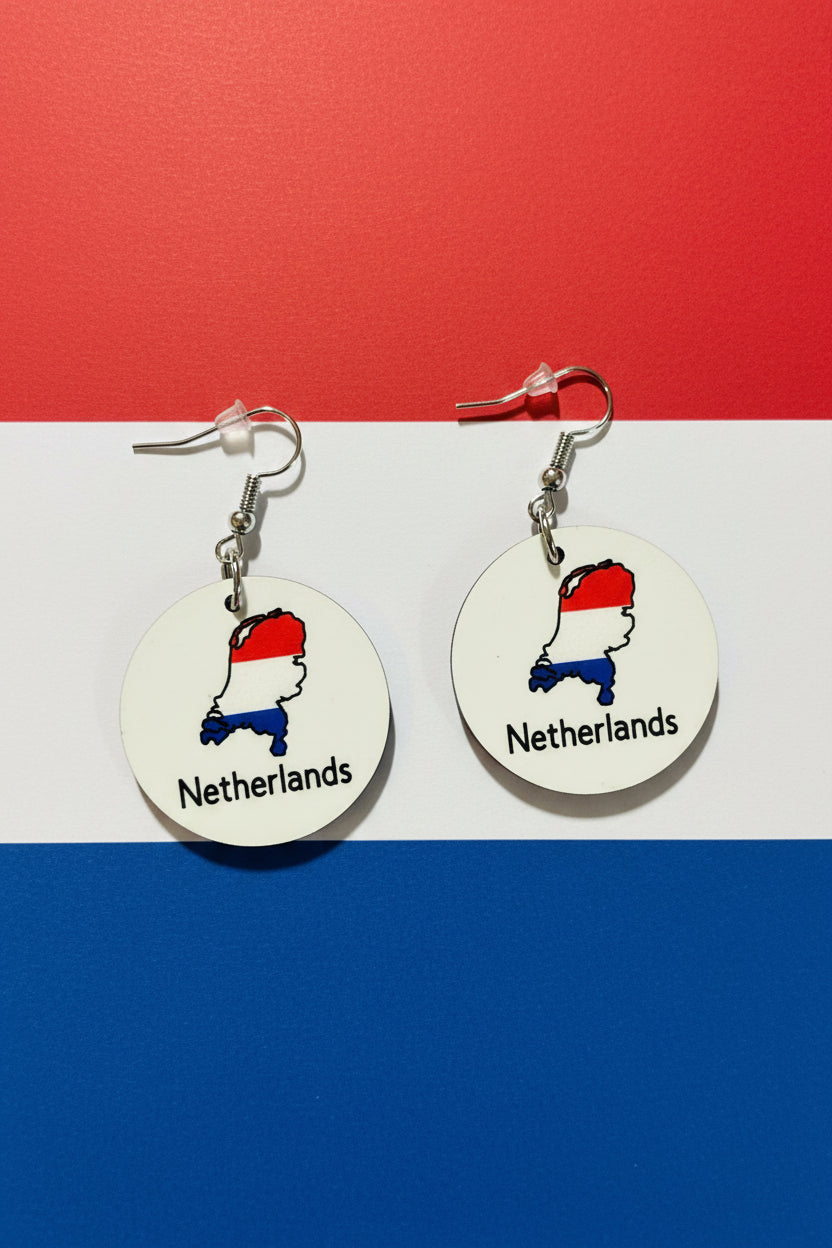 A pair of circular earrings featuring the Netherlands map in red, white, and blue, displayed on a background matching the Dutch flag colors.