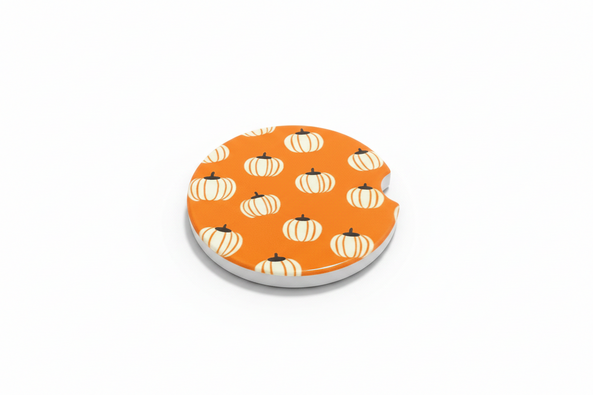 A round ceramic car coaster with repeating pattern of white pumpkins with orange stripes and black stems, shown on a clean white background. Roxzell