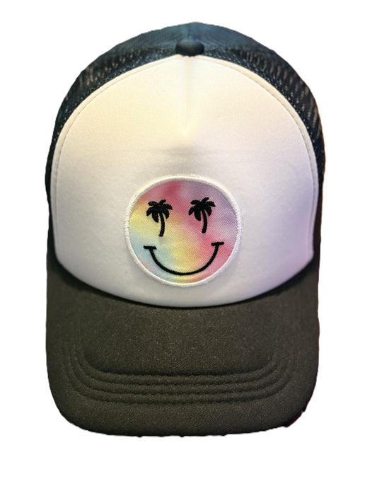 Front view of a black and white trucker hat featuring a colorful smiley face patch with palm tree eyes and a curved black brim.