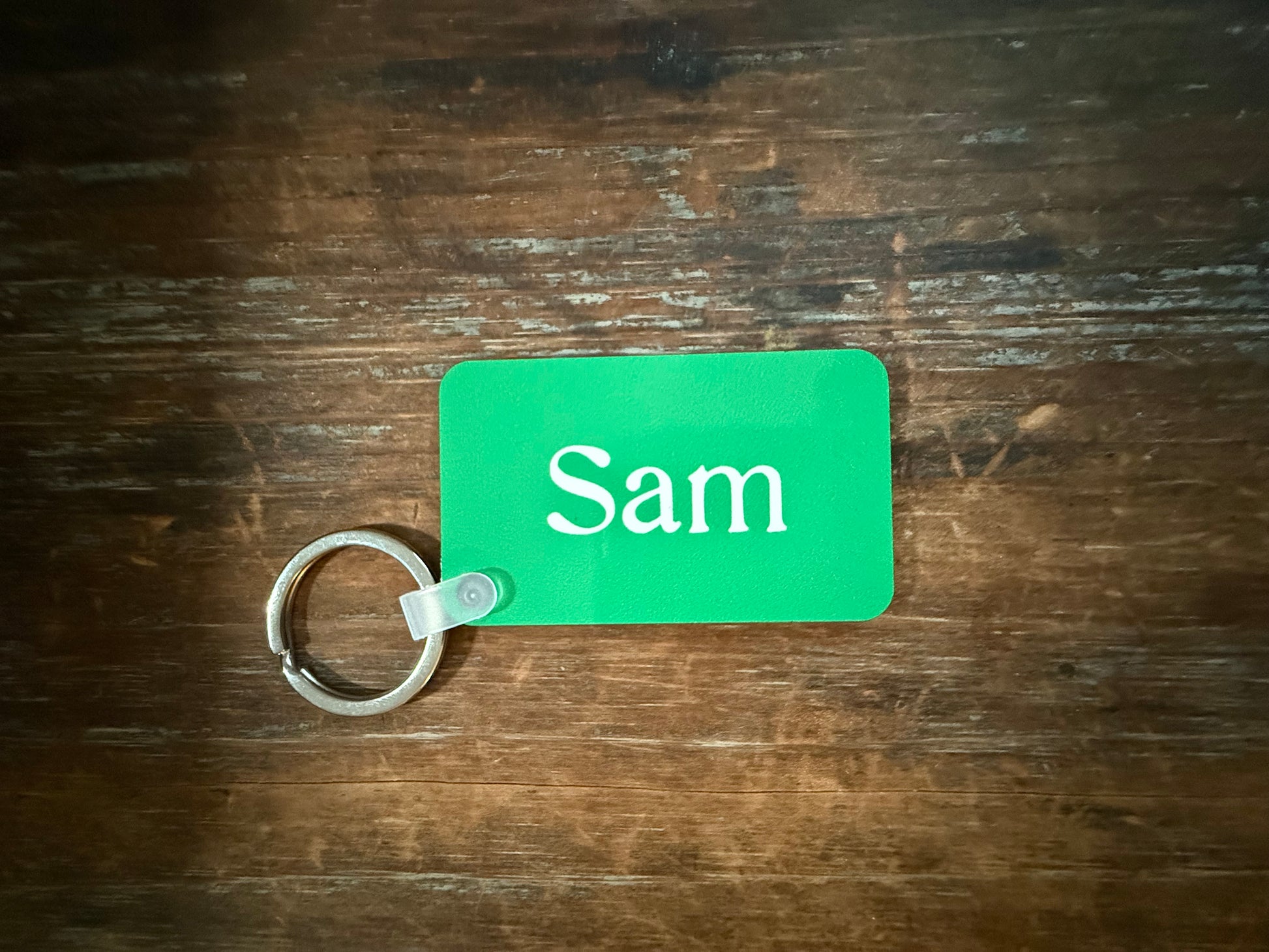 Yellow keychain with custom name “Sam” attached to silver ring on wood surface. Roxzell