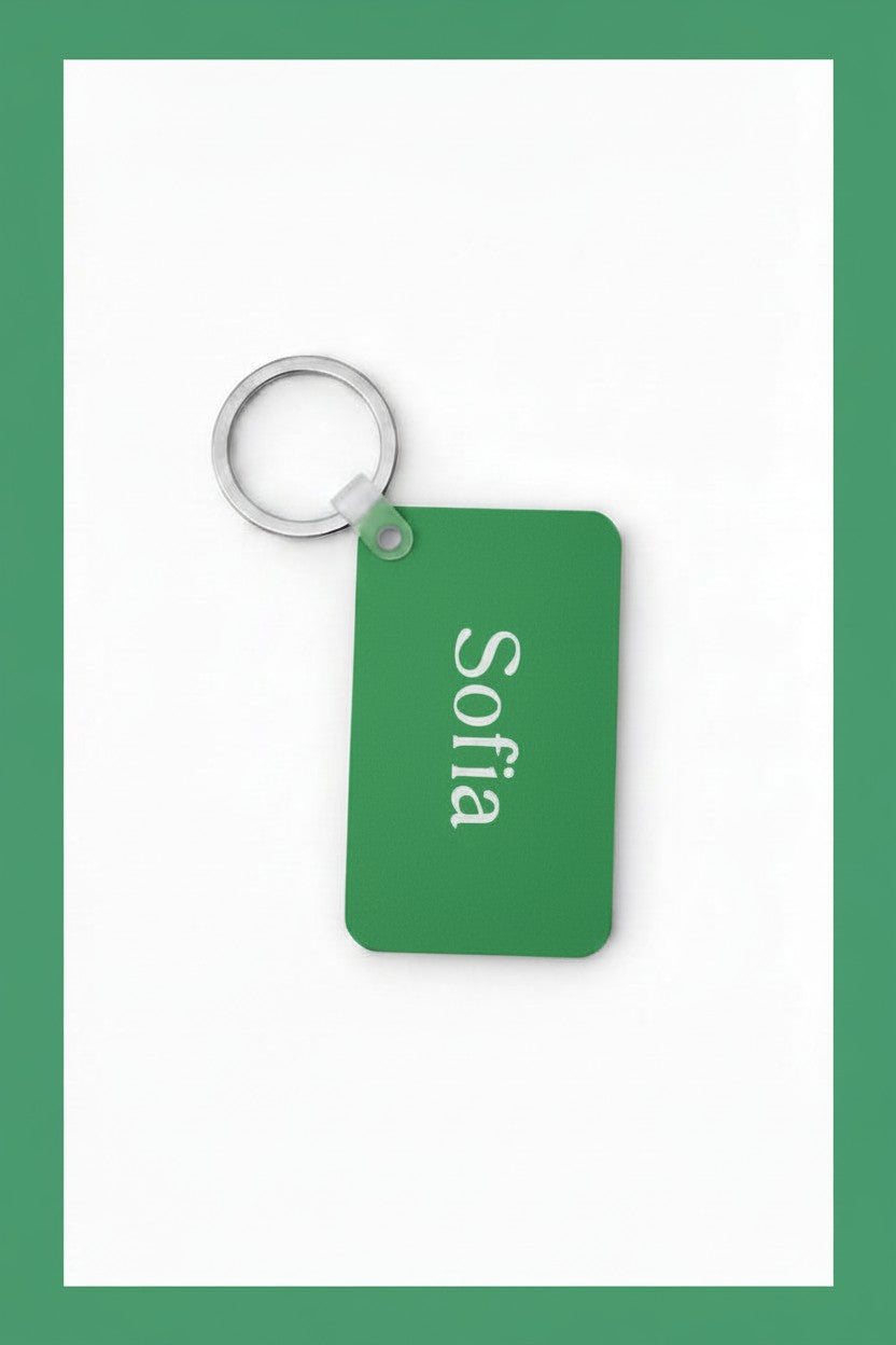 A rectangular green keychain tag with rounded corners, attached to a silver metal split ring. The tag is printed with the name 'Sofia' in white vertical text, set against a white background with a teal border. Roxzell