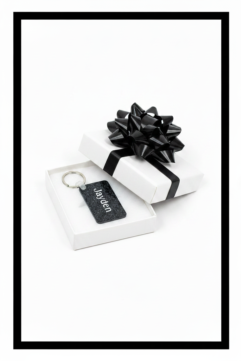 Personalized keychain with name Jayden in white in a white gift box with a black bow on a white background with a black border. Roxzell