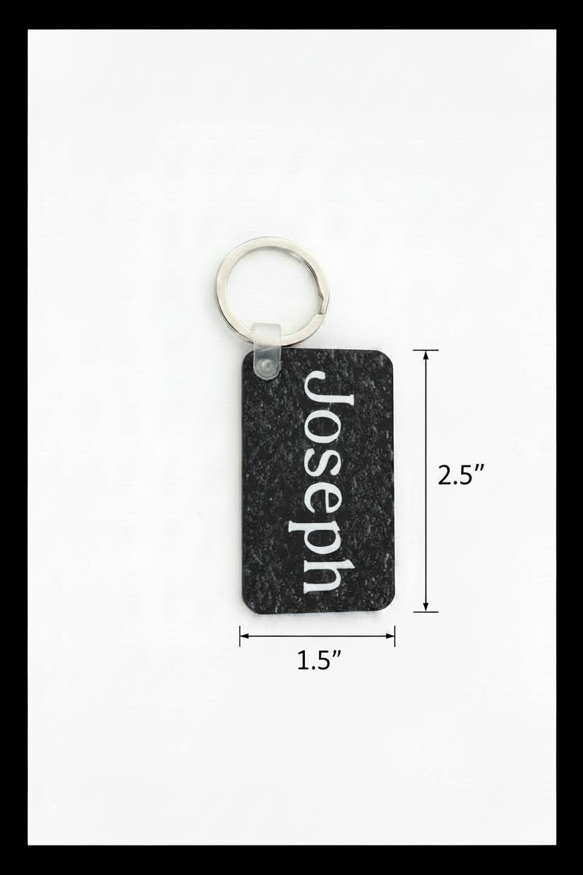 A rectangular black textured keychain with the name 'Joseph' printed vertically in white, attached to a silver metal key ring. A dimension line below indicates the size is 1.5" wide and 2.5" long. Roxzell