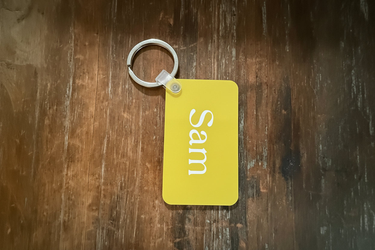Yellow keychain with custom name “Sam” attached to silver ring on wood surface. Roxzell