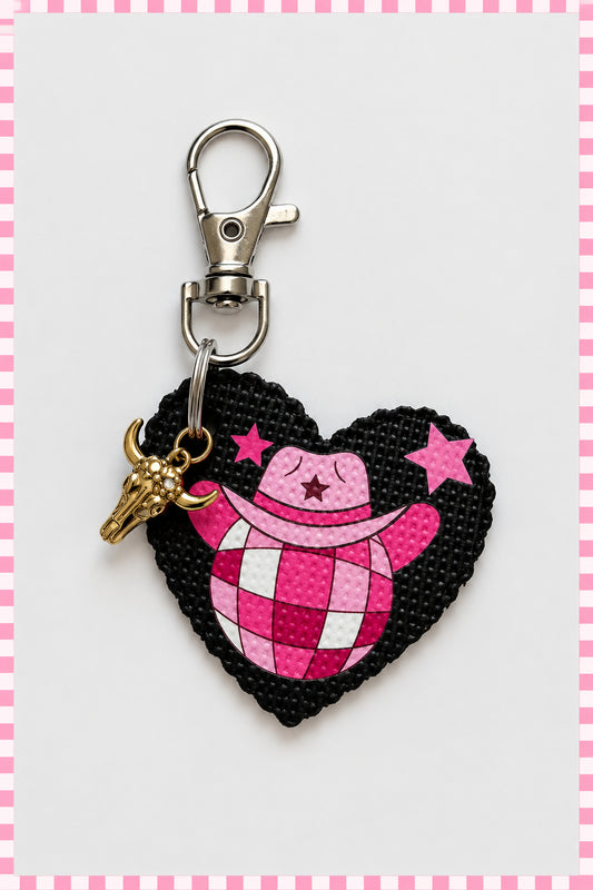 A heart-shaped leather keychain charm featuring a pink and white gingham pattern with a cowboy hat, pink stars, and a small gold-tone bull head charm, attached to a silver lobster clasp on a plain light background with pink and white border. Roxzell