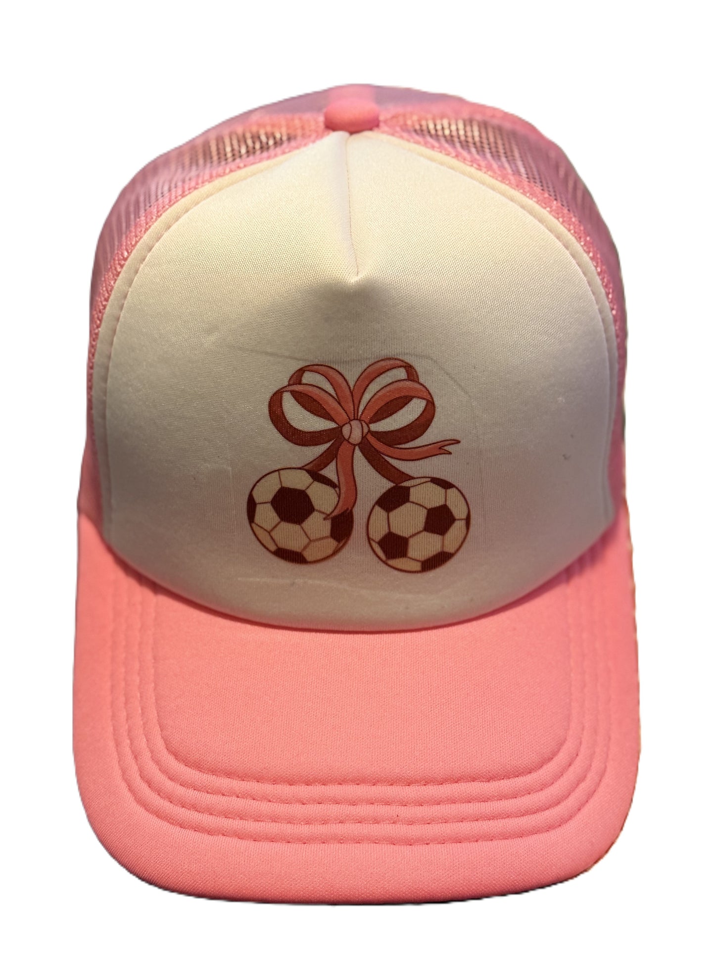 A pink and white trucker-style cap featuring two brown soccer balls tied with a pink ribbon bow on the front panel. Roxzell