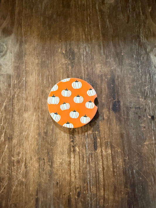 A round orange car coaster with a white and orange pumpkin pattern, placed on a dark brown wooden surface. Roxzell