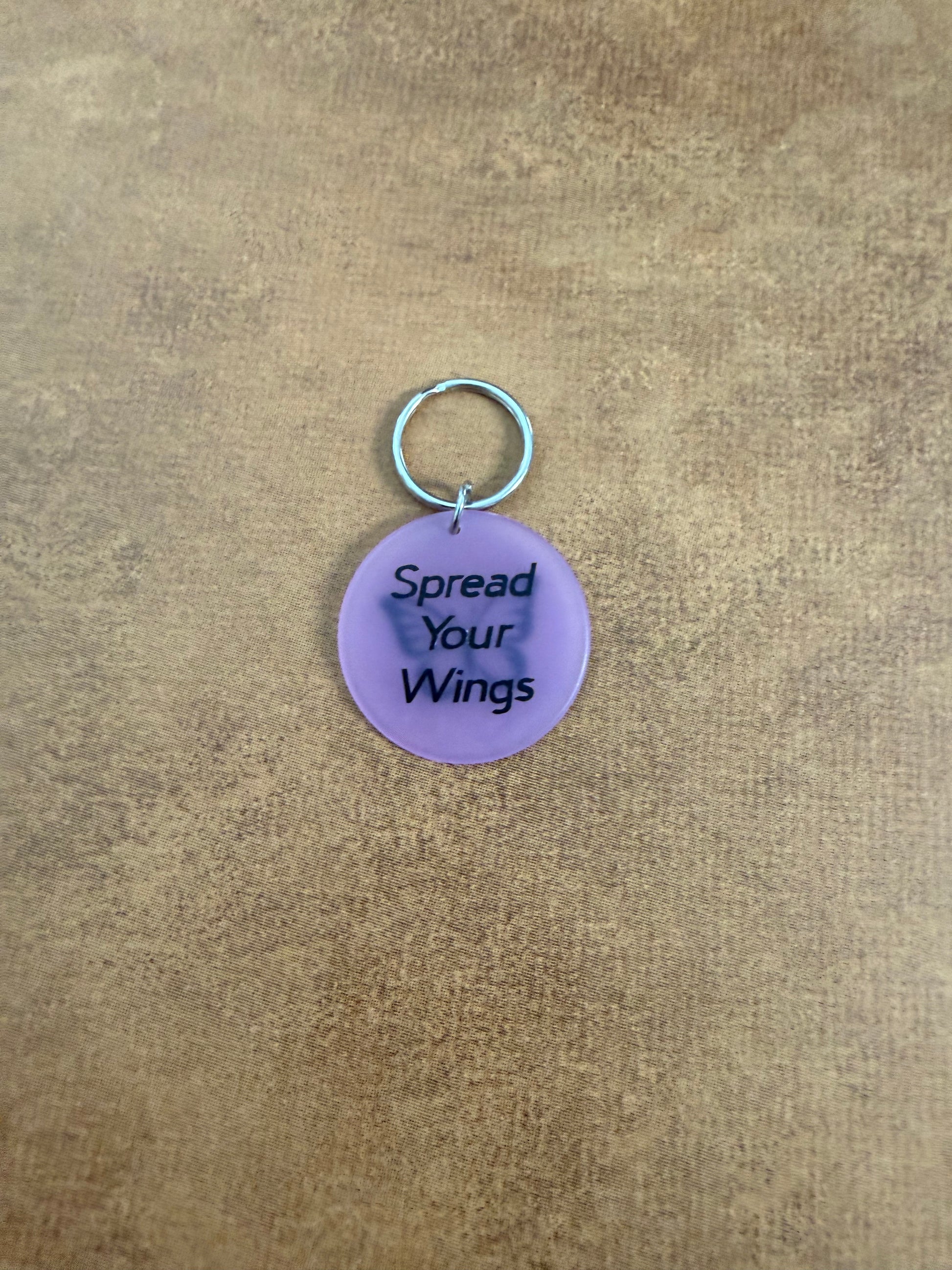 Purple acrylic butterfly keychain with "Spread Your Wings" on the reverse side.