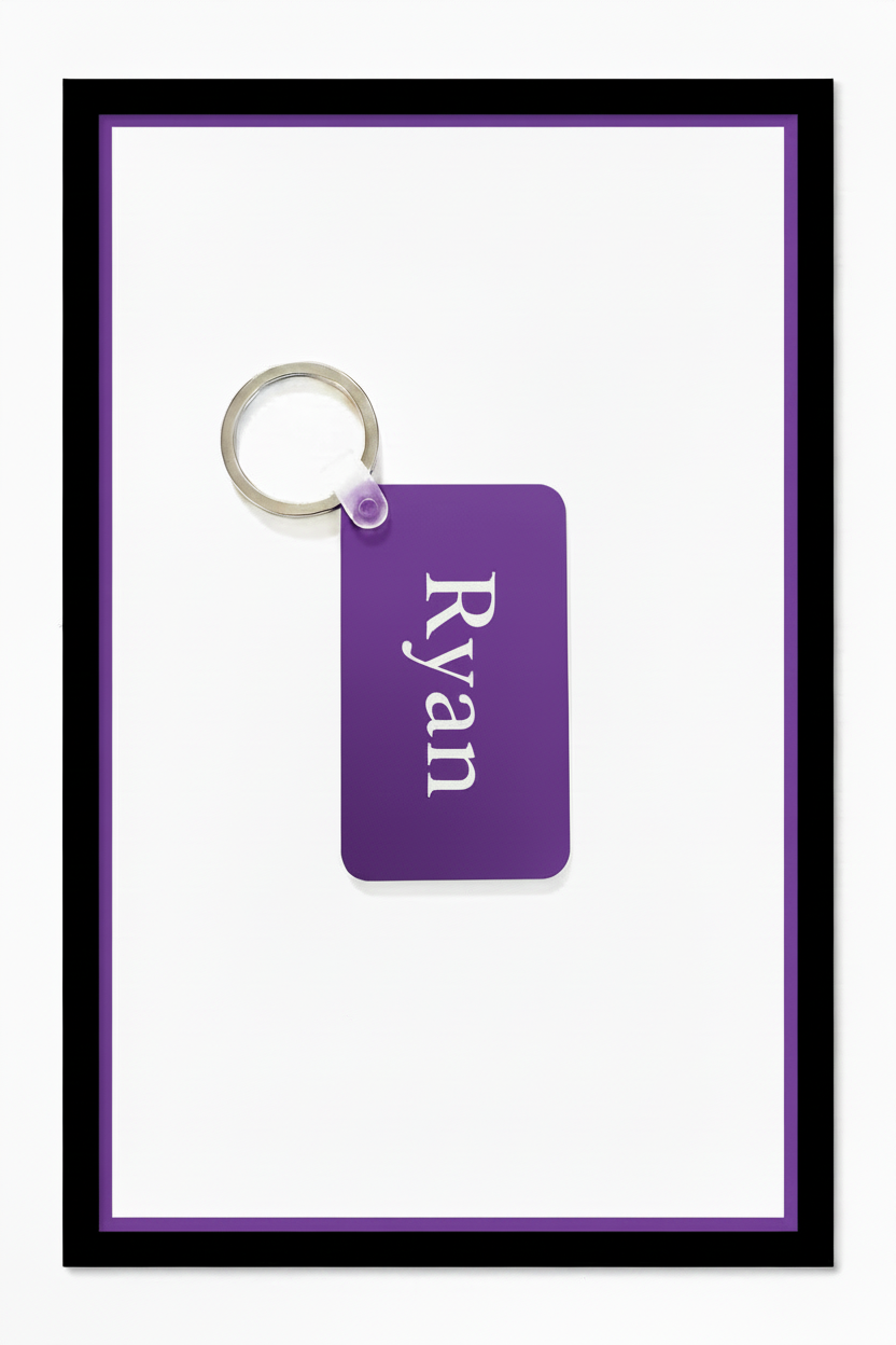 A personalized purple rectangular keychain tag with the name 'Ryan' printed in white serif text, attached to a silver metal key ring, set against a white background with a purple inner border and black outer frame. Roxzell