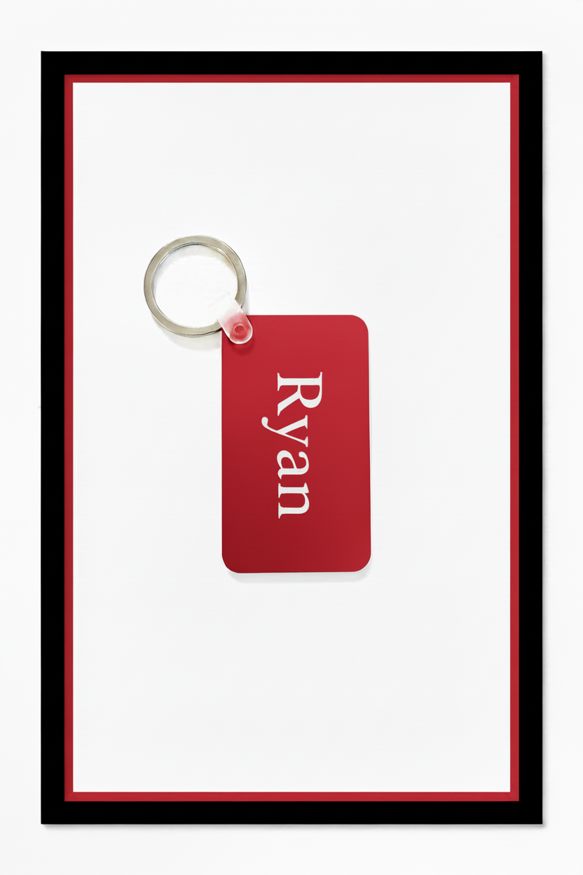 A personalized red rectangular keychain tag with the name 'Ryan' printed in white serif text, attached to a silver metal key ring, set against a white background with a red inner border and black outer frame. Roxzell