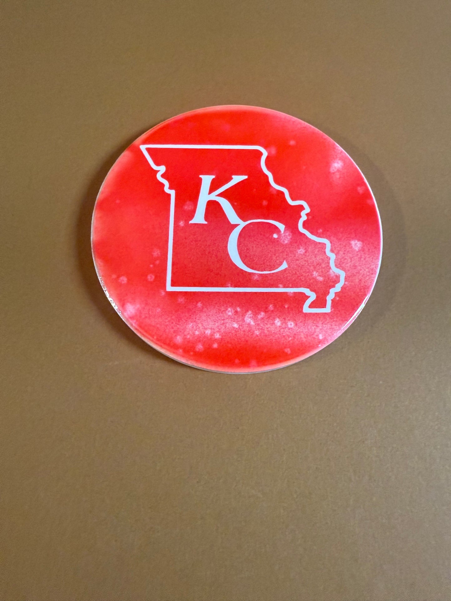 Red and white round ceramic coaster with KC designed inside the shape of Missouri.