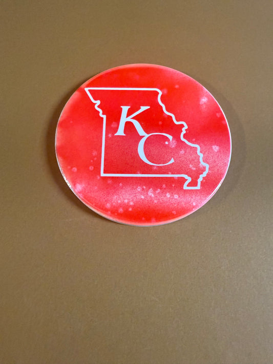 Red and white round ceramic coaster with KC designed inside the shape of Missouri.