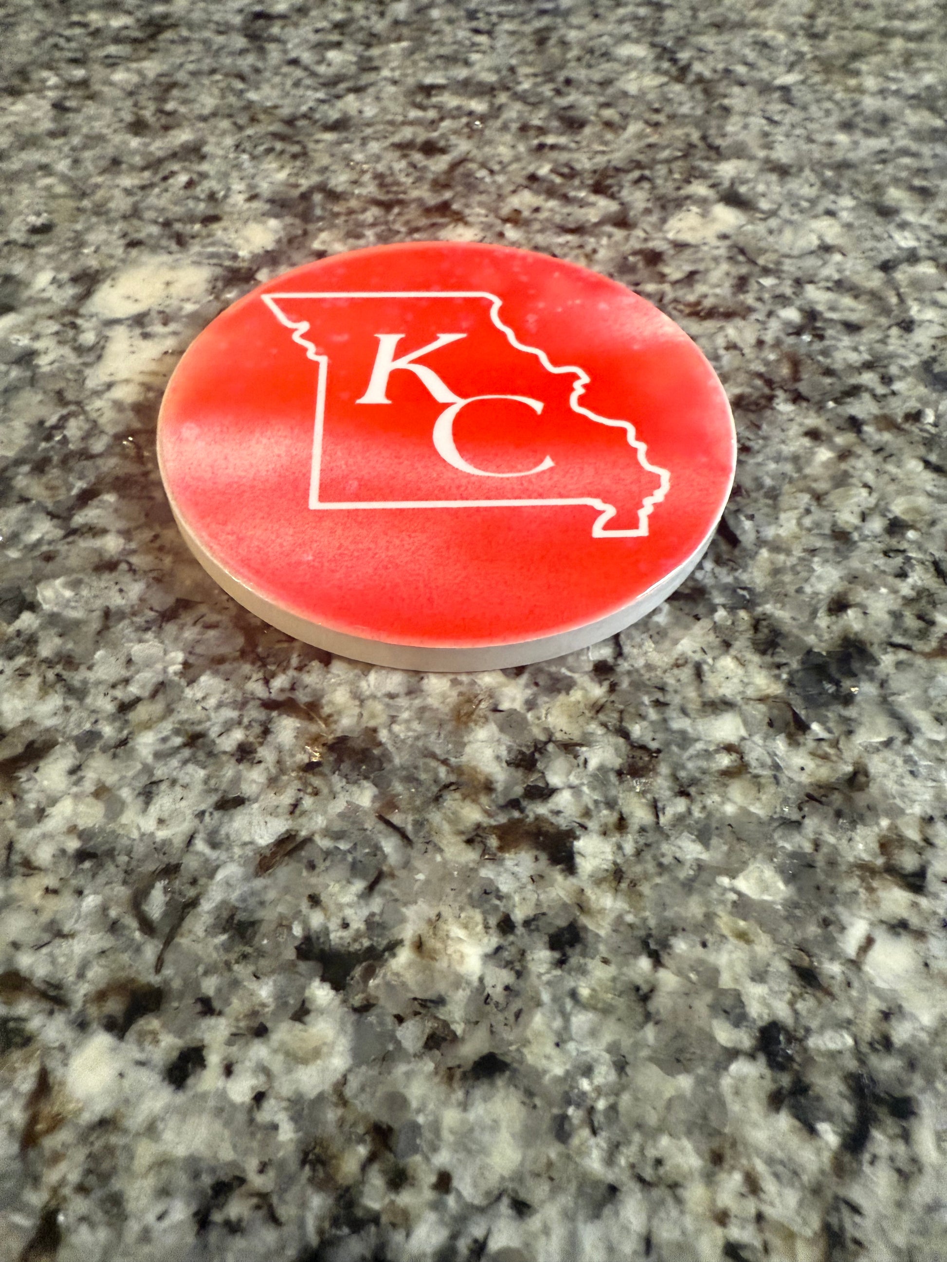 Red and white round ceramic coaster with KC designed inside the shape of Missouri.