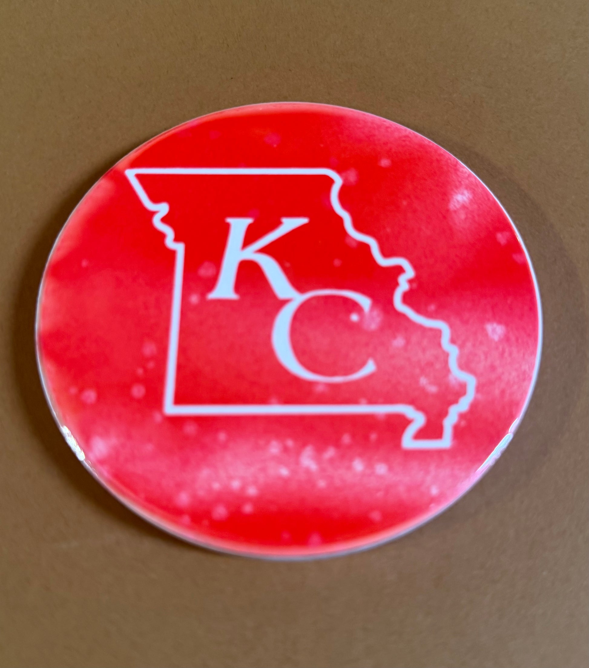 Red and white round ceramic coaster with KC designed inside the shape of Missouri.