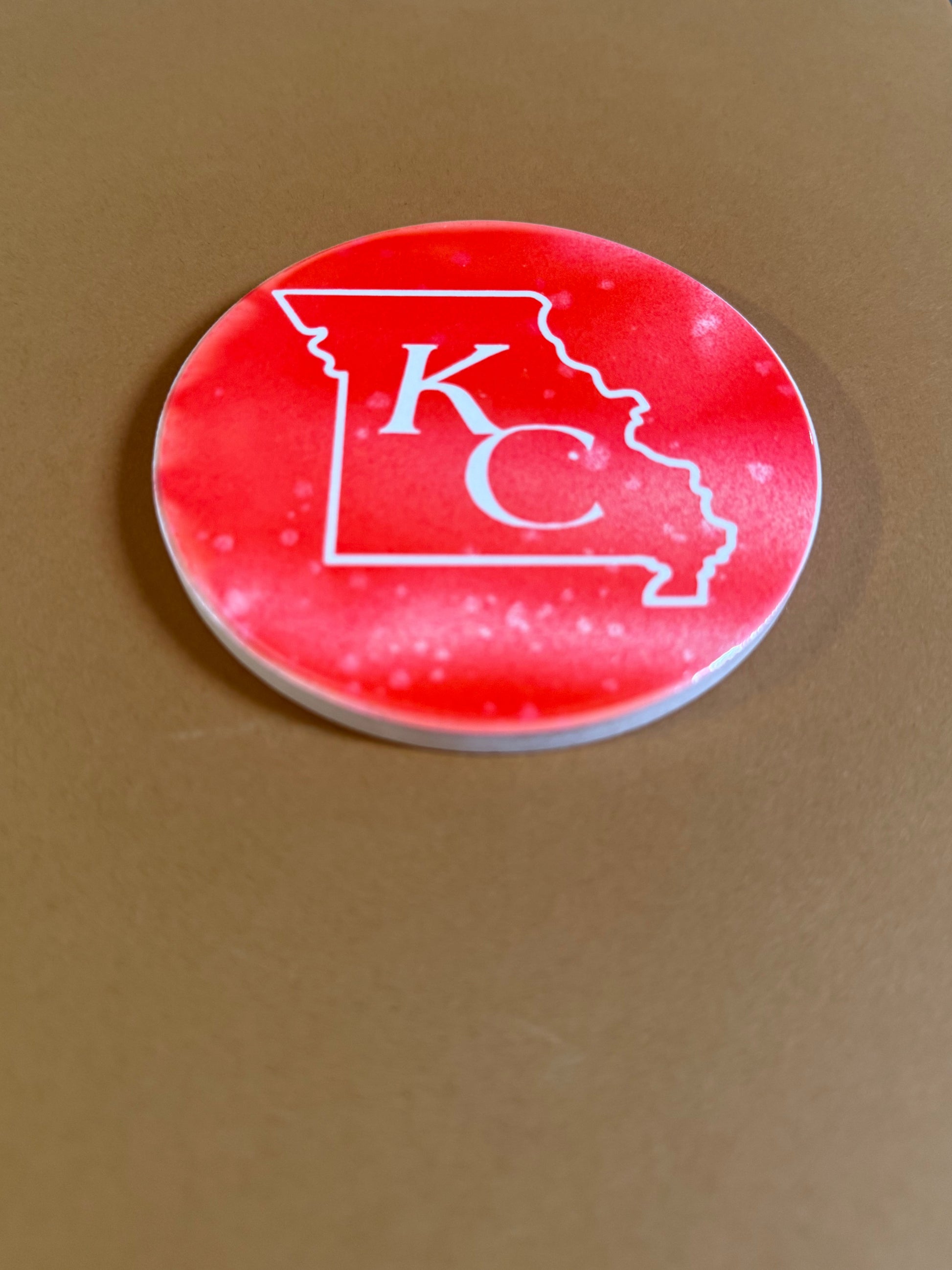 Red and white round ceramic coaster with KC designed inside the shape of Missouri.