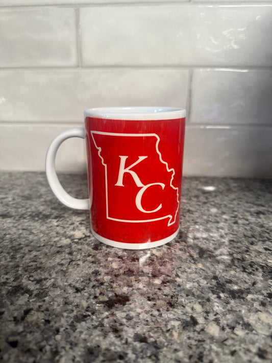 A red ceramic mug with 'KC' monogram in white, placed on a kitchen countertop.