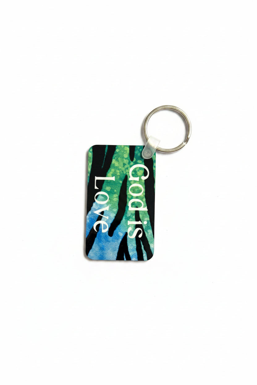A rectangular keychain with a silver split ring, featuring a colorful abstract design of green, blue, and black brushstrokes with the words 'God Is Love' printed vertically in white on a white background. Roxzell
