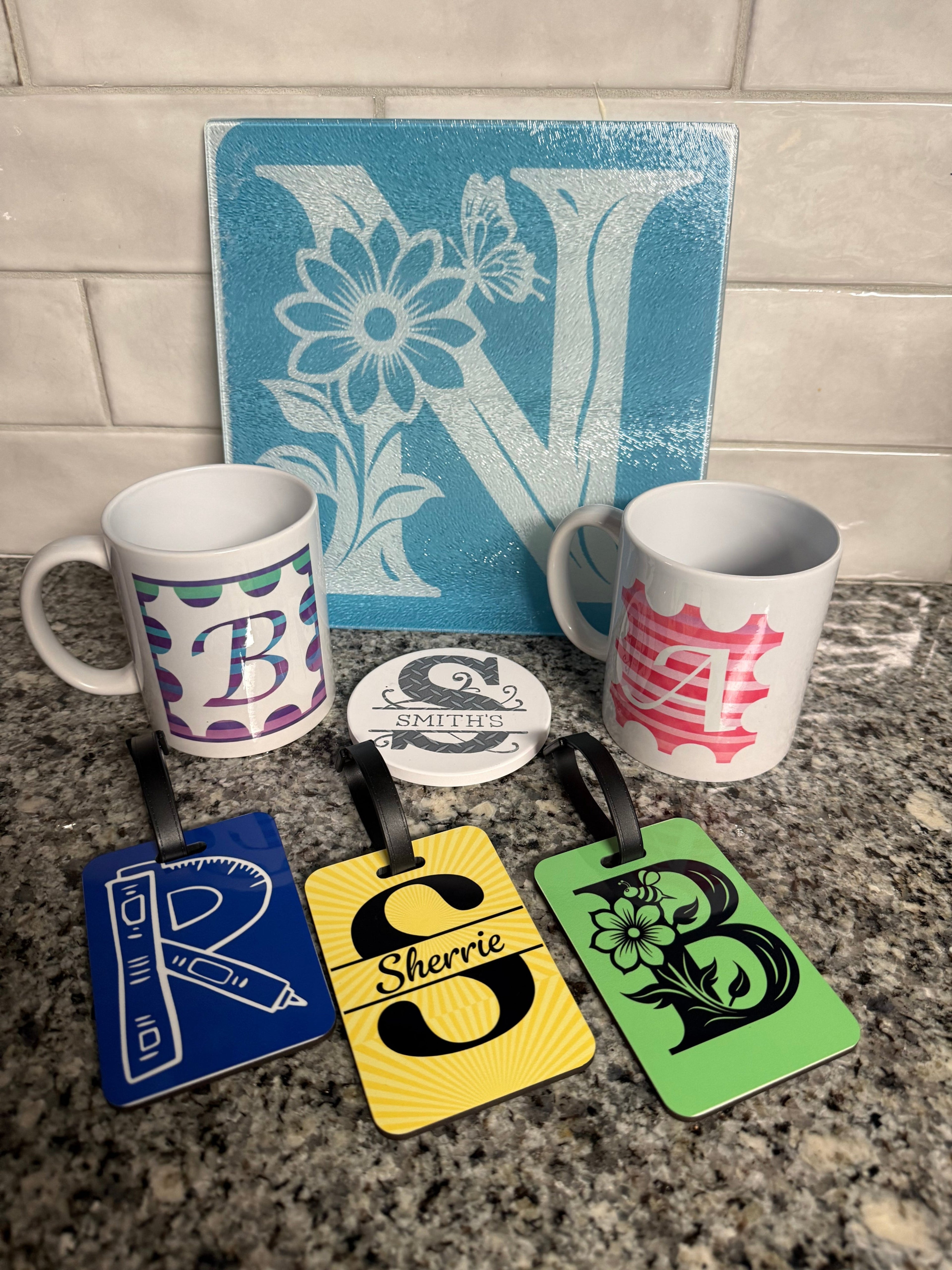 Glass cutting board with personalized letter 'N', white ceramic mug with blue, green and purple personalized letter 'B', personalized luggage tags, letter 'S' personalized coaster, and personalized mug with pink letter 'A', Roxzell