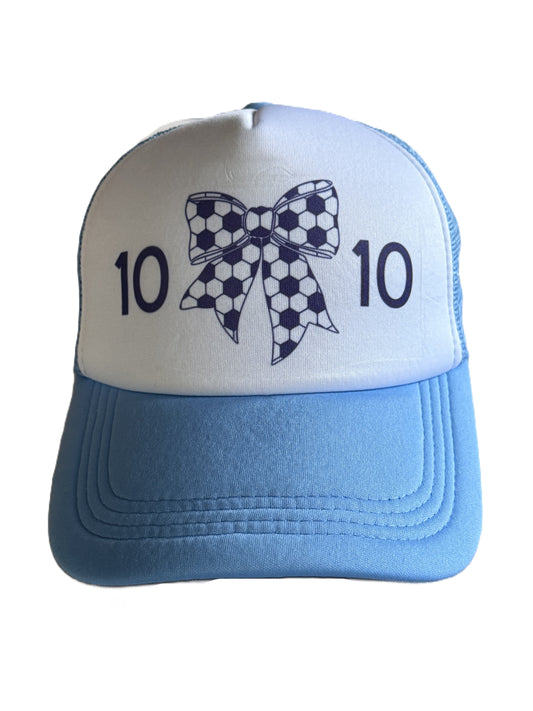 A light blue and white trucker hat featuring a soccer-themed bow graphic on the front with the number 10 on each side.
